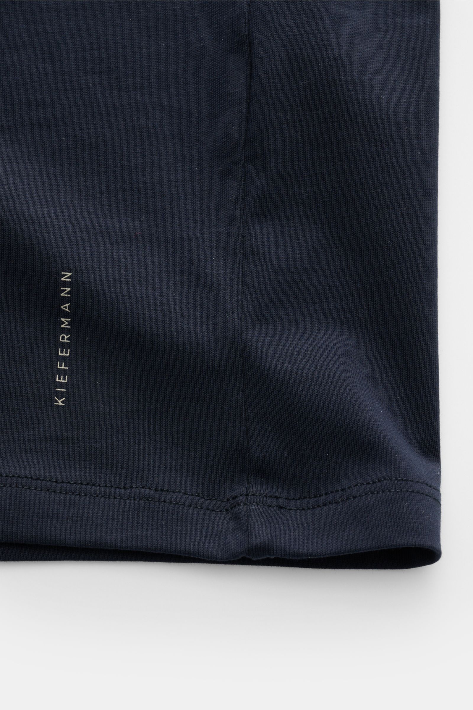 Nahaufnahme des unteren Bereichs vom Kiefermann Rundhals T-Shirt 'Matello' navy, Extra Slim Fit aus weichem Baumwoll-Jersey mit glattem Griff und dezentem Logodruck am Saum, von oben fotografiert.