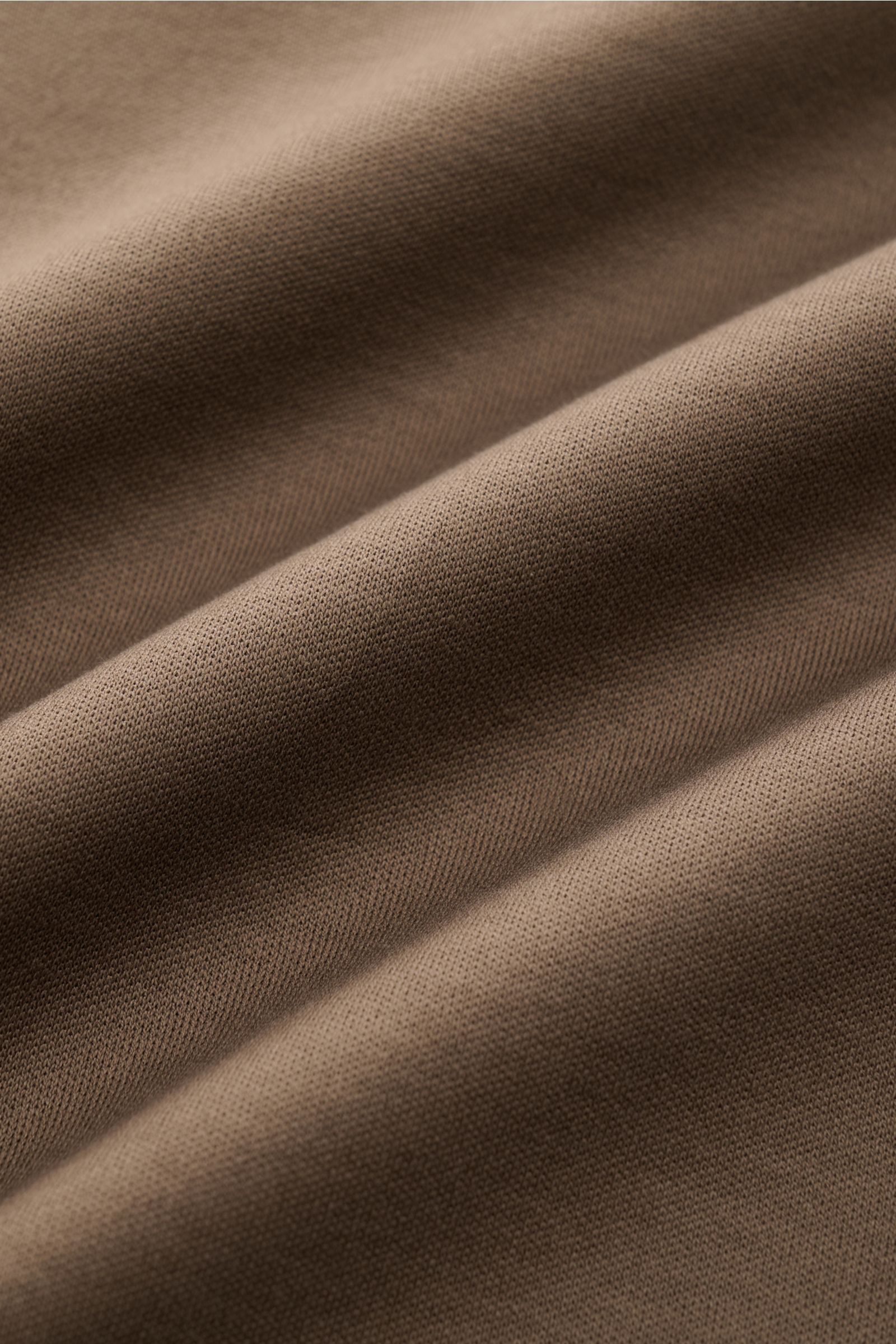 Close-up image of the fabric texture of the Aurélien Rundhals-T-Shirt khaki, photographed from a top-down angle, showing jersey made from Egyptian cotton with a soft, smooth feel, slim fit, round neckline, short hem slits, and subtle logo stitching on the