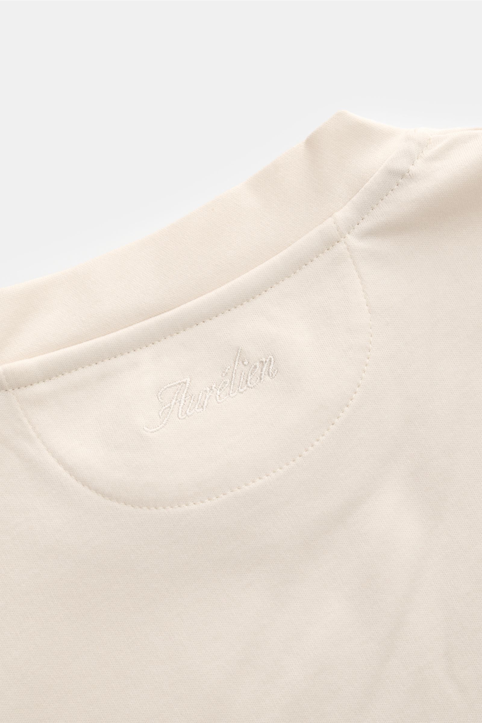 Close-up image of the back neckline of the Aurélien Rundhals-T-Shirt sand, photographed from above, showing subtle logo stitching. Jersey aus ägyptischer Baumwolle, weicher, glatter Griff, Slim Fit, Rundhalsausschnitt, kurze Saumschlitze, dezentes Logo-St