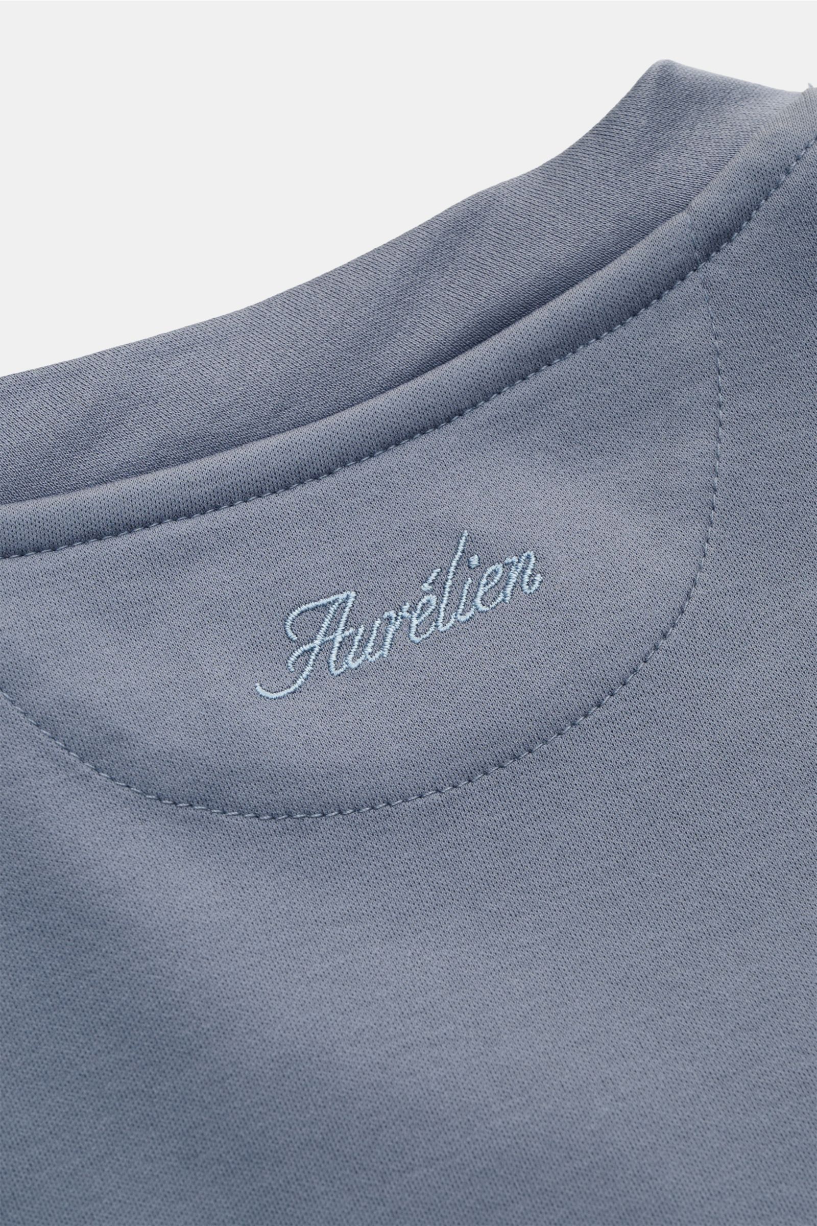 Nahaufnahme des Aurélien Rundhals-T-Shirts rauchblau aus reiner Baumwolle mit weichem Griff, Slim Fit, Rundhalsausschnitt und kurzen Saumschlitzen, fotografiert von schräg oben.