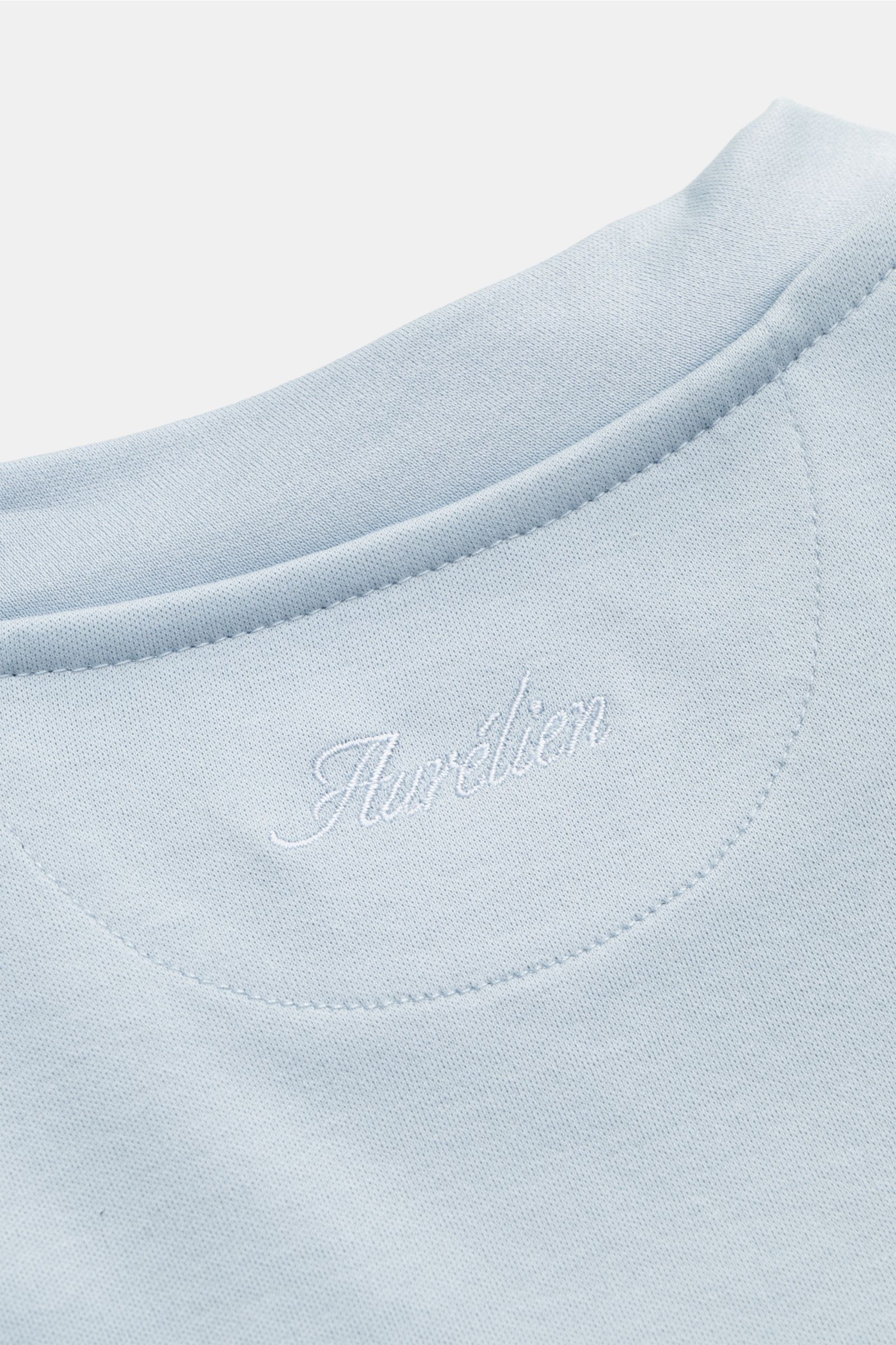 Close-up front view of the Aurélien Rundhals-T-Shirt hellblau, showing light blue fabric and embroidered Aurélien logo at the neckline. Vielseitiges Basic für den Frühling und Sommer: Das T-Shirt von AURÉLIEN verbindet hochwertige Baumwollqualität mit kla