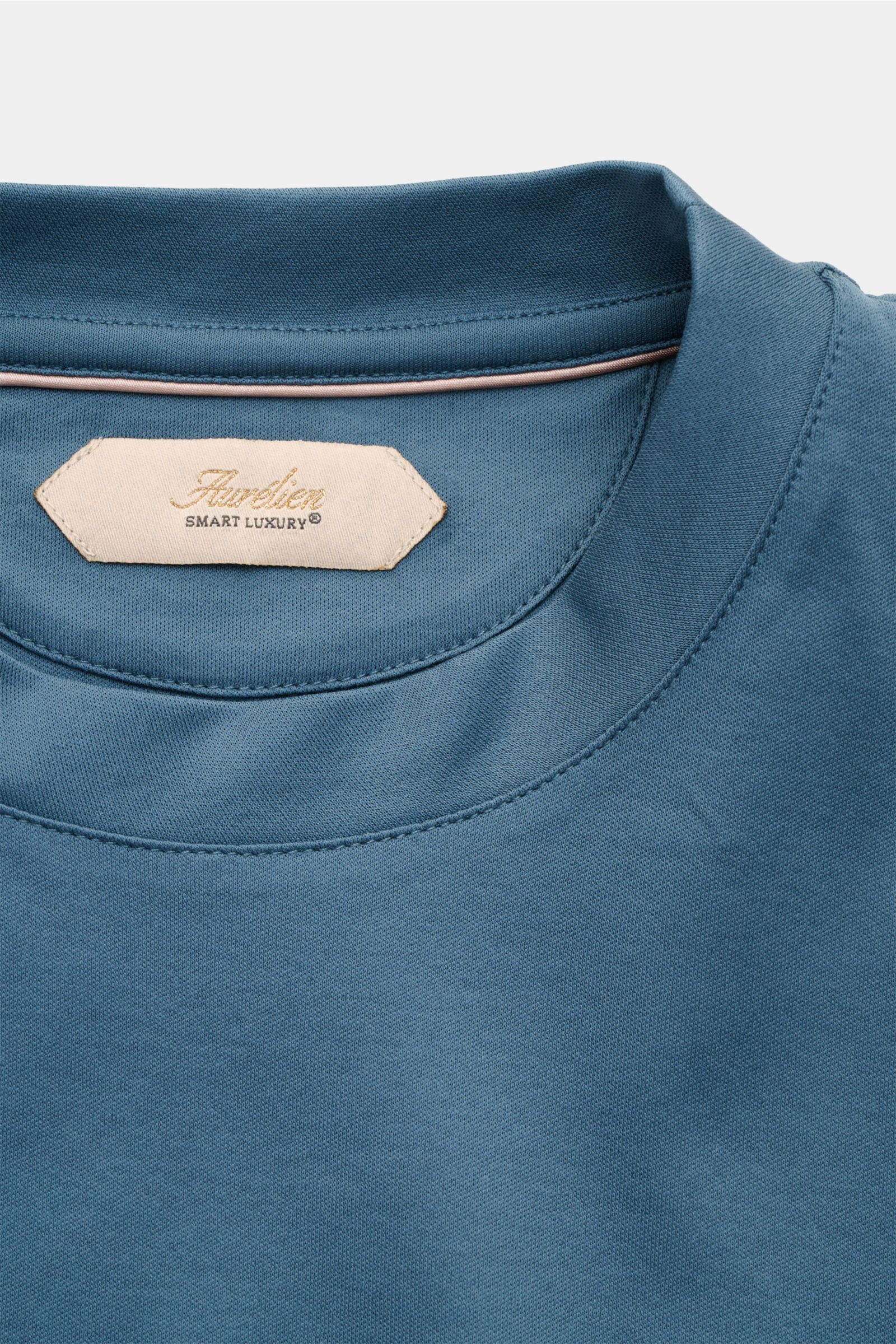 Nahaufnahme des Aurélien Rundhals-T-Shirts petrol von oben, reine Baumwolle, weicher Griff, Slim Fit, Rundhalsausschnitt, tonales Logo-Stitching, kurze Saumschlitze.
