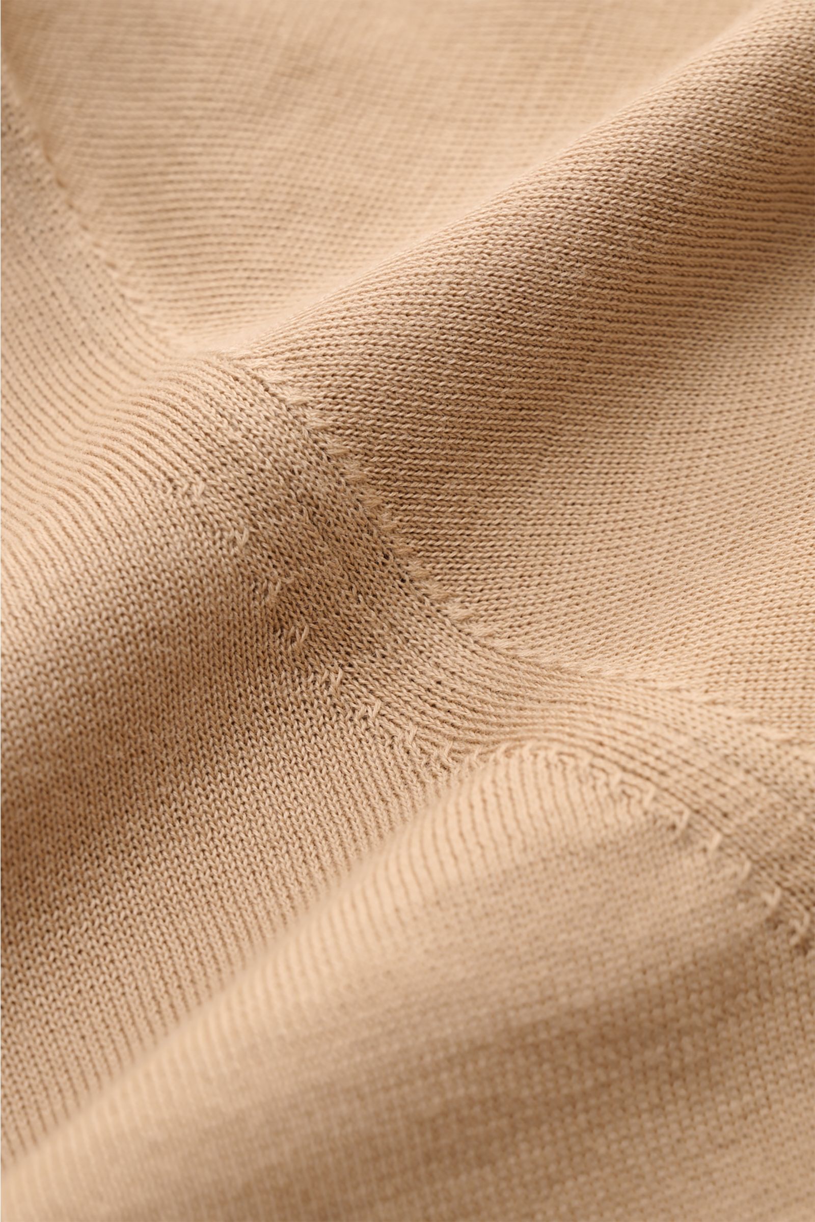 Nahaufnahme des hellbraunen Drumohr Kurzarmpullovers aus feinem, weichem Baumwollstrick mit feinem Strickbild, elastischen Rippbündchen, fotografiert aus schräger Perspektive.