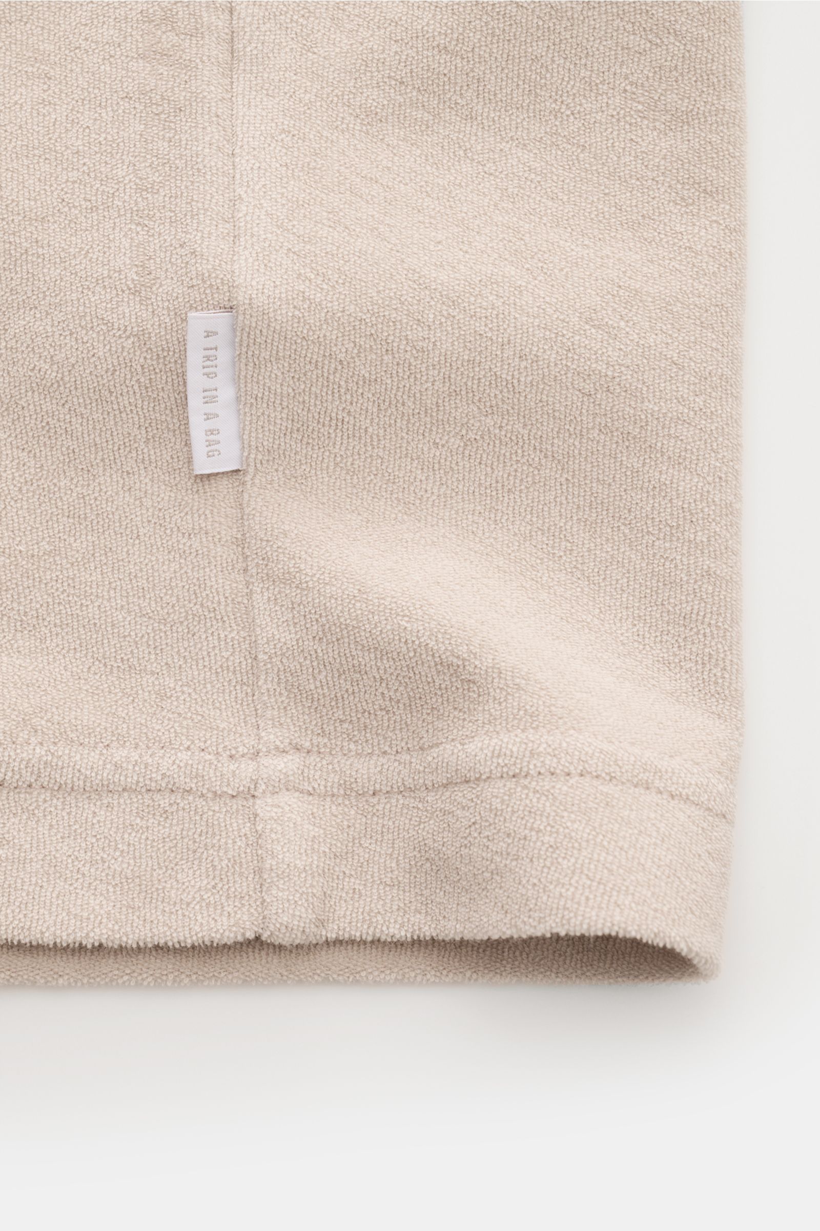 Close-up view of the hem and side seam of the 04651/ A trip in a bag Terry T-shirt 'Terry Tee' beige, showing soft pure cotton terrycloth fabric with a small woven label.

The clean T-shirt 'Terry Tee' by 04651/ A TRIP IN A BAG is made of soft terry in