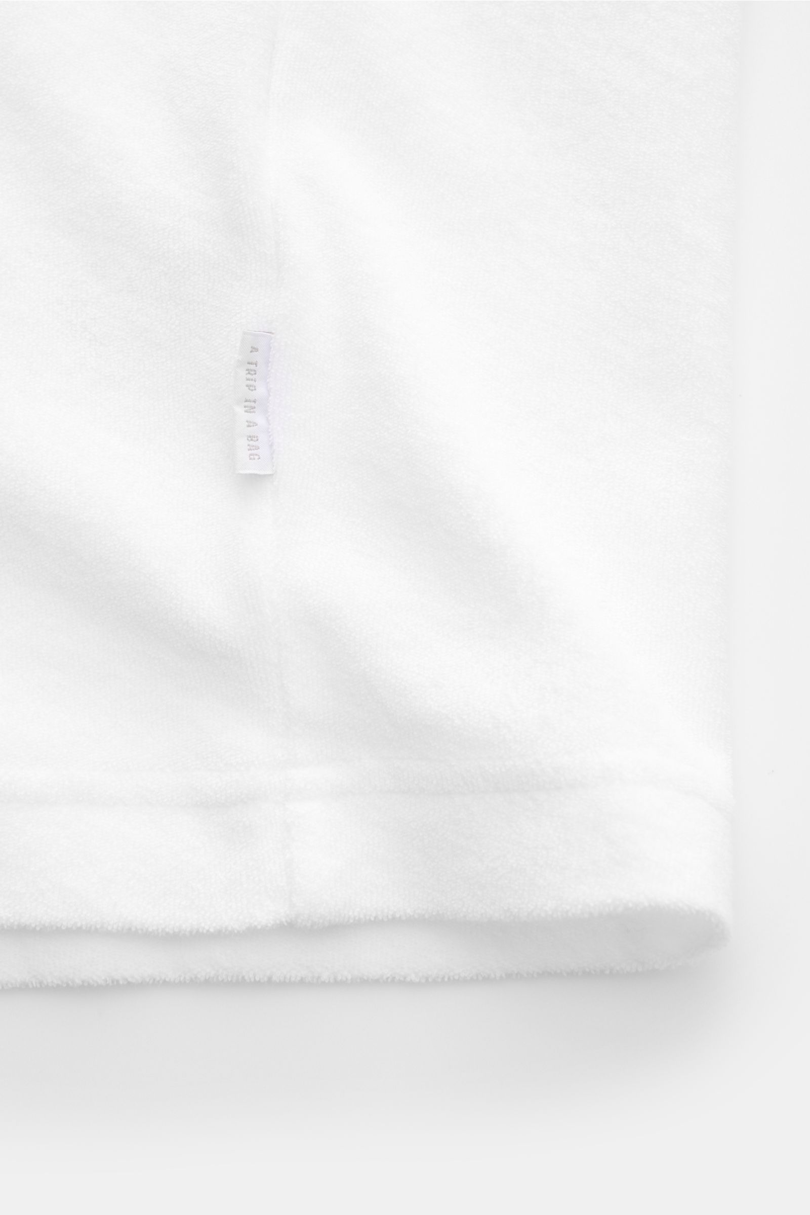 Close-up view of the hem and side seam with a small woven label of the 04651/ A trip in a bag Terry T-shirt 'Terry Tee' white, made of soft pure cotton terrycloth.

The clean T-shirt 'Terry Tee' by 04651/ A TRIP IN A BAG is made of soft terry in pure c