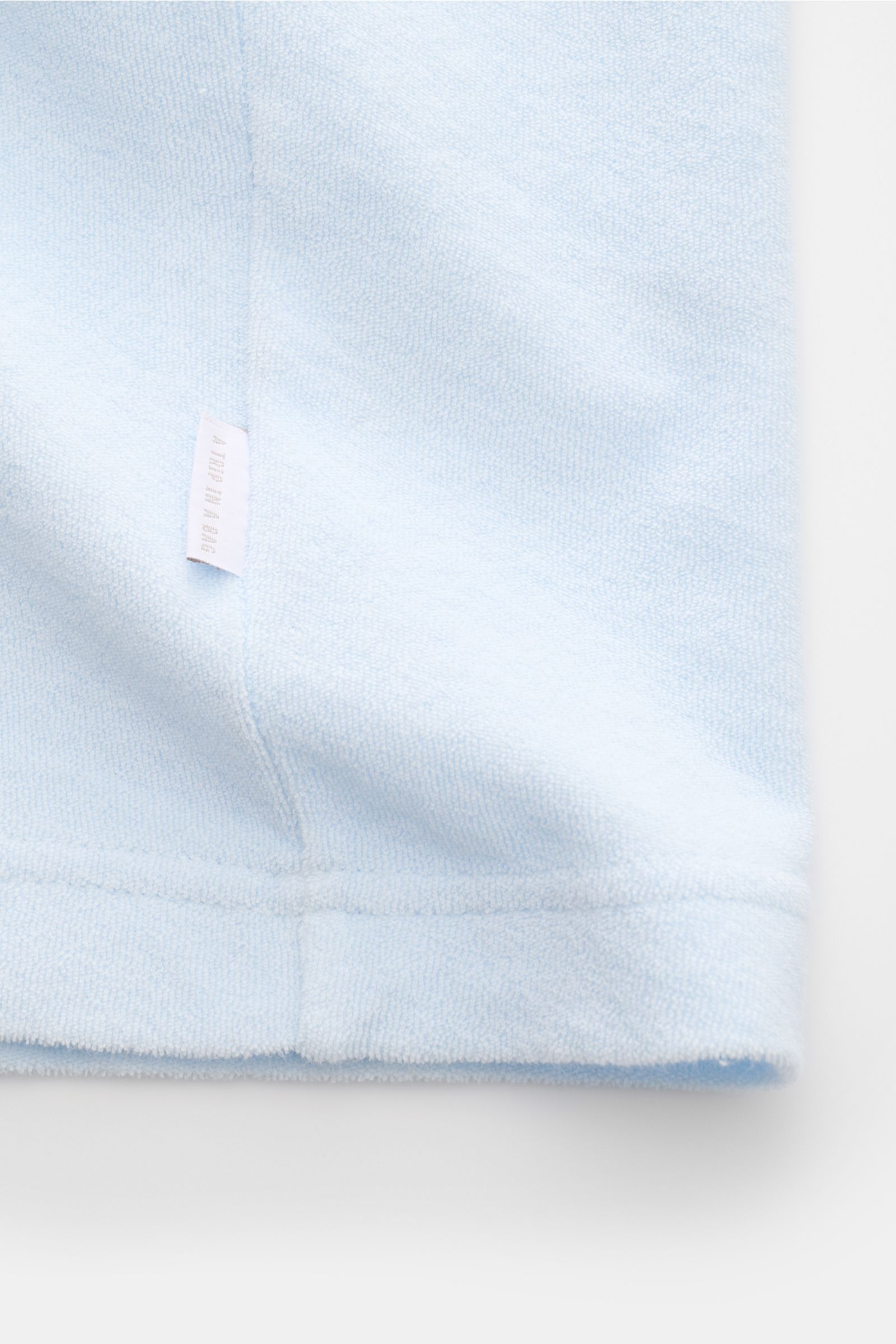 Close-up bottom hem view of 04651/ A trip in a bag Terry T-shirt 'Terry Tee' pastel blue made of soft pure cotton terrycloth with a small woven label in the side seam. The clean T-shirt 'Terry Tee' by 04651/ A TRIP IN A BAG is made of soft terry in pure c