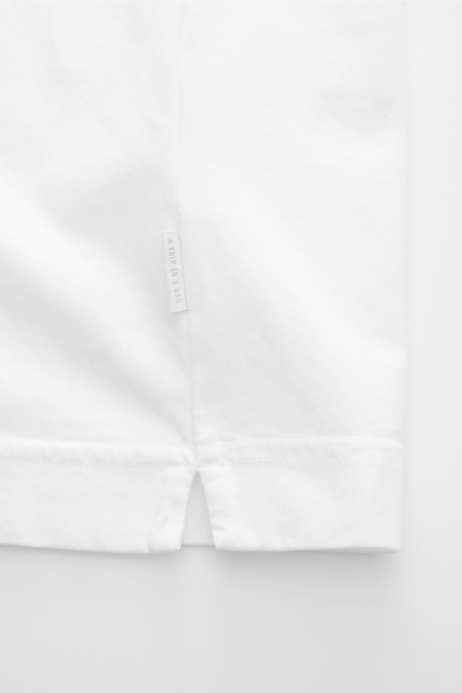 04651/ A trip in a bag Rundhals-T-Shirt weiß, Detailaufnahme des unteren Saums mit kurzem Schlitz, Jersey aus reiner Baumwolle, weicher Griff, Regular Fit, kleines Weblabel.