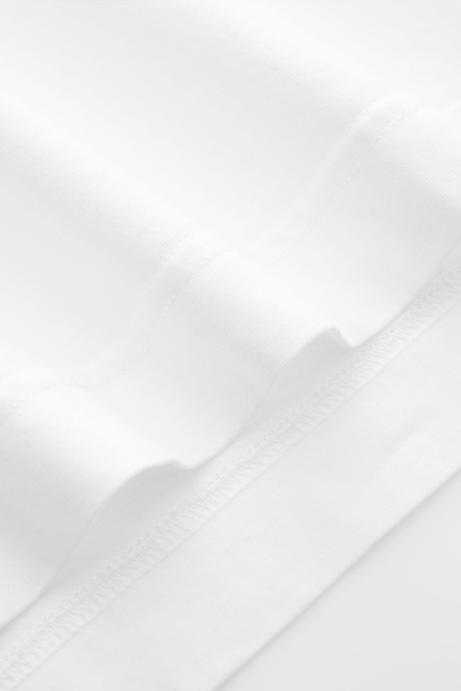 Nahaufnahme des weißen 04651/ A trip in a bag Rundhals-T-Shirts mit Jersey aus reiner Baumwolle, weichem Griff, Regular Fit, Rundhalsausschnitt, kleinem Weblabel und kurzen Saumschlitzen, fotografiert von unten.