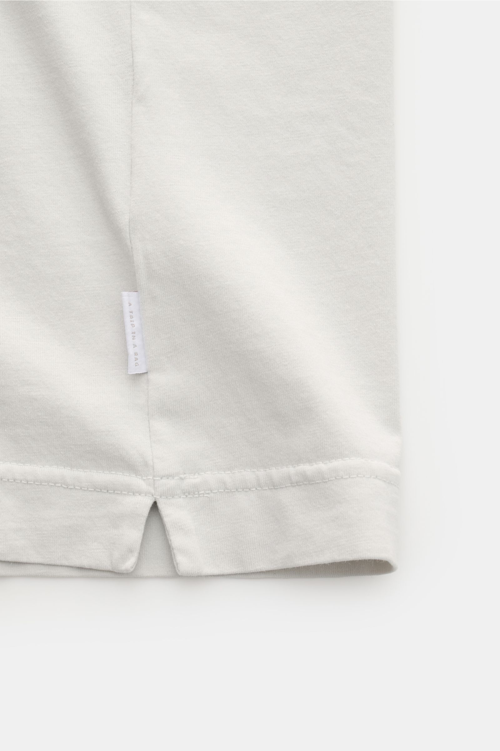 Detailaufnahme des Saum-Bereichs von 04651/ A trip in a bag Rundhals-T-Shirt hellgrau, Jersey aus reiner Baumwolle, weicher Griff, Regular Fit, Rundhalsausschnitt, kleines Weblabel sichtbar.