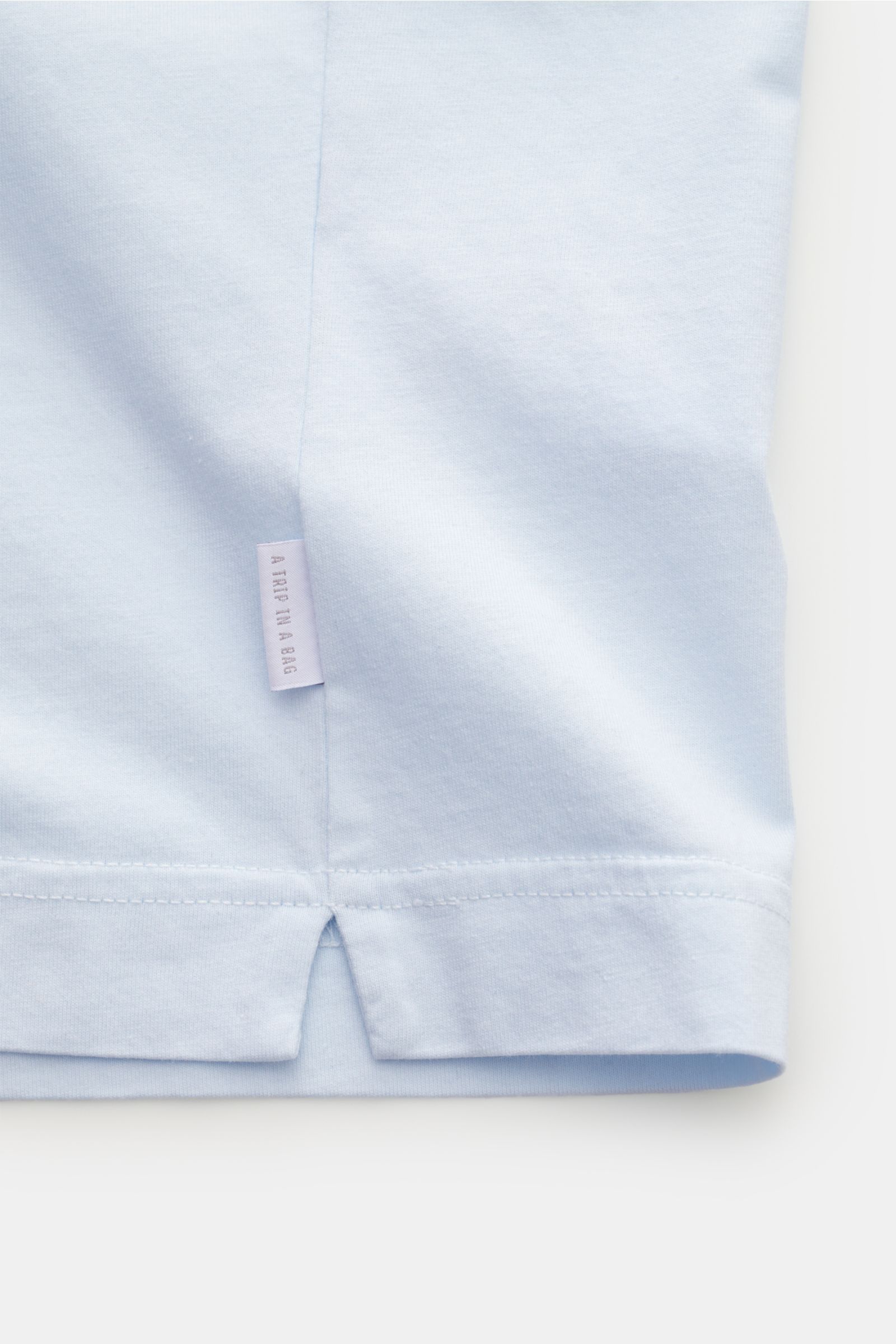 04651/ A trip in a bag Rundhals-T-Shirt pastellblau, Detailansicht Saum mit kleinem Weblabel, Jersey aus reiner Baumwolle, weicher Griff, Regular Fit, Rundhalsausschnitt.