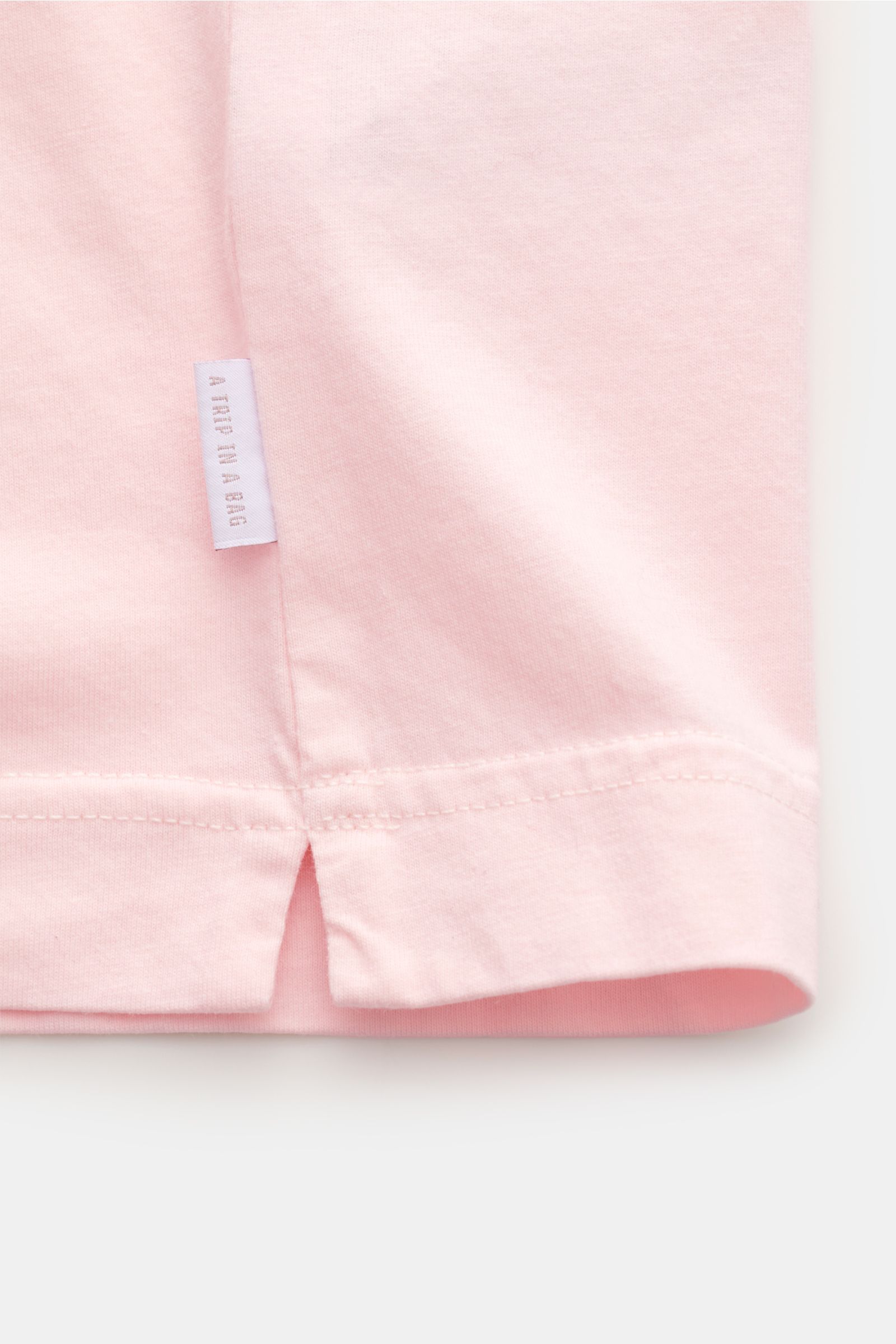 Nahaufnahme des unteren Saums des 04651/ A trip in a bag Rundhals-T-Shirts rosé, Jersey aus reiner Baumwolle, weicher Griff, Regular Fit, Rundhalsausschnitt, kleines Weblabel an der Seitennaht, fotografiert von vorne unten.