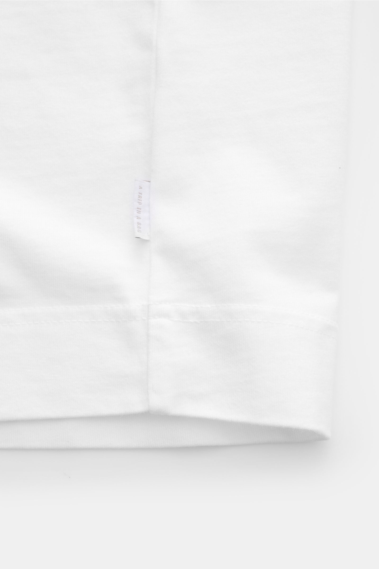 04651/ A trip in a bag Rundhals-T-Shirt weiß, Detailaufnahme unten, robustes Baumwoll-Jersey, schwere Qualität, kleines Weblabel am Saum.