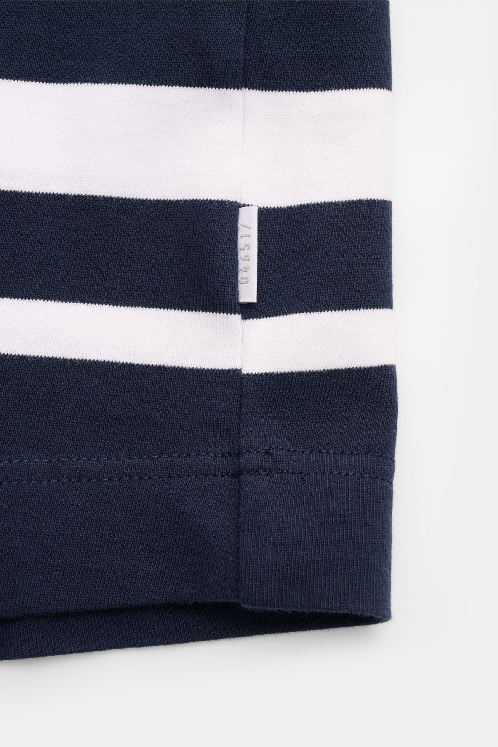 Nahaufnahme des Details eines 04651/ A trip in a bag Rundhals-T-Shirts 'Nunu' navy/weiß gestreift mit kleinem Weblabel, schwerer Baumwollqualität, weichem Griff und Regular Fit, fotografiert frontal auf weißem Hintergrund.
