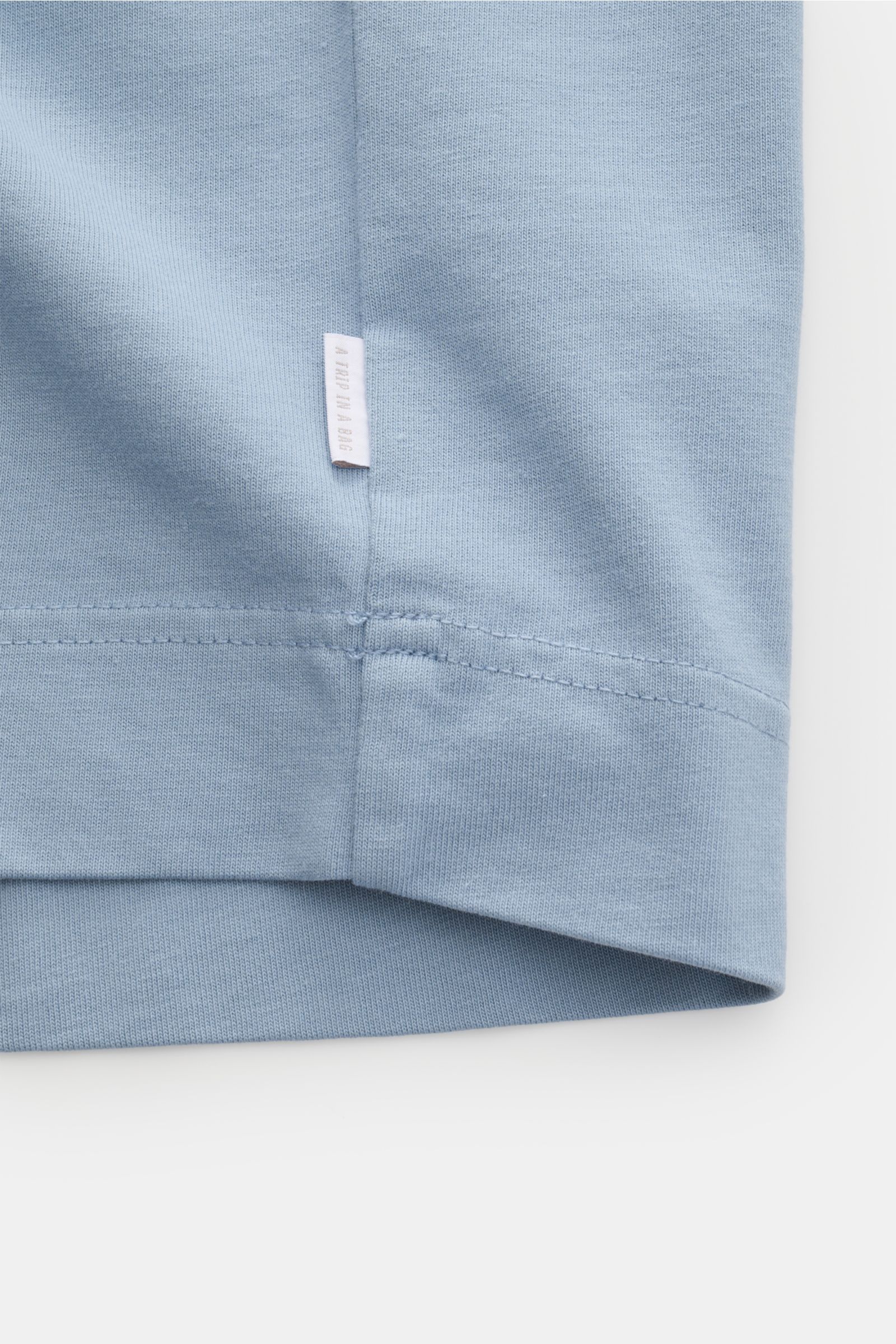 Close-up back view of the hem and side seam of the 04651/ A trip in a bag T-shirt 'Nunu' smoky blue, showing fabric texture and a small label.

Description: 
A basic with a print accent: With its minimalist holiday print, this T-shirt by 04651/ A TRIP 
