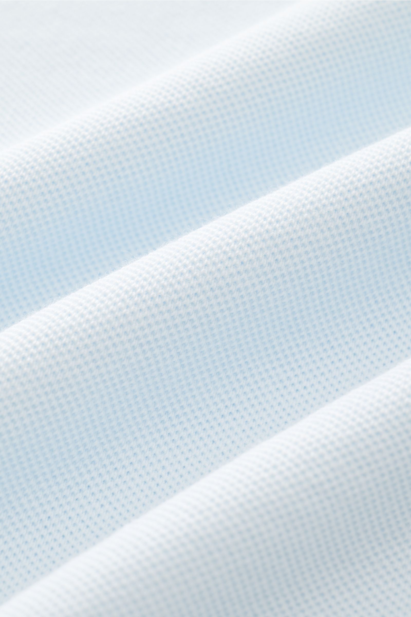 Close-up of pastel blue fabric texture showing fine piqué knit with soft folds, photographed from a macro perspective. The 04651/ A trip in a bag Piqué T-shirt pastel blue is a summer essential: This piqué T-shirt from 04651/ A TRIP IN A BAG is a versatil