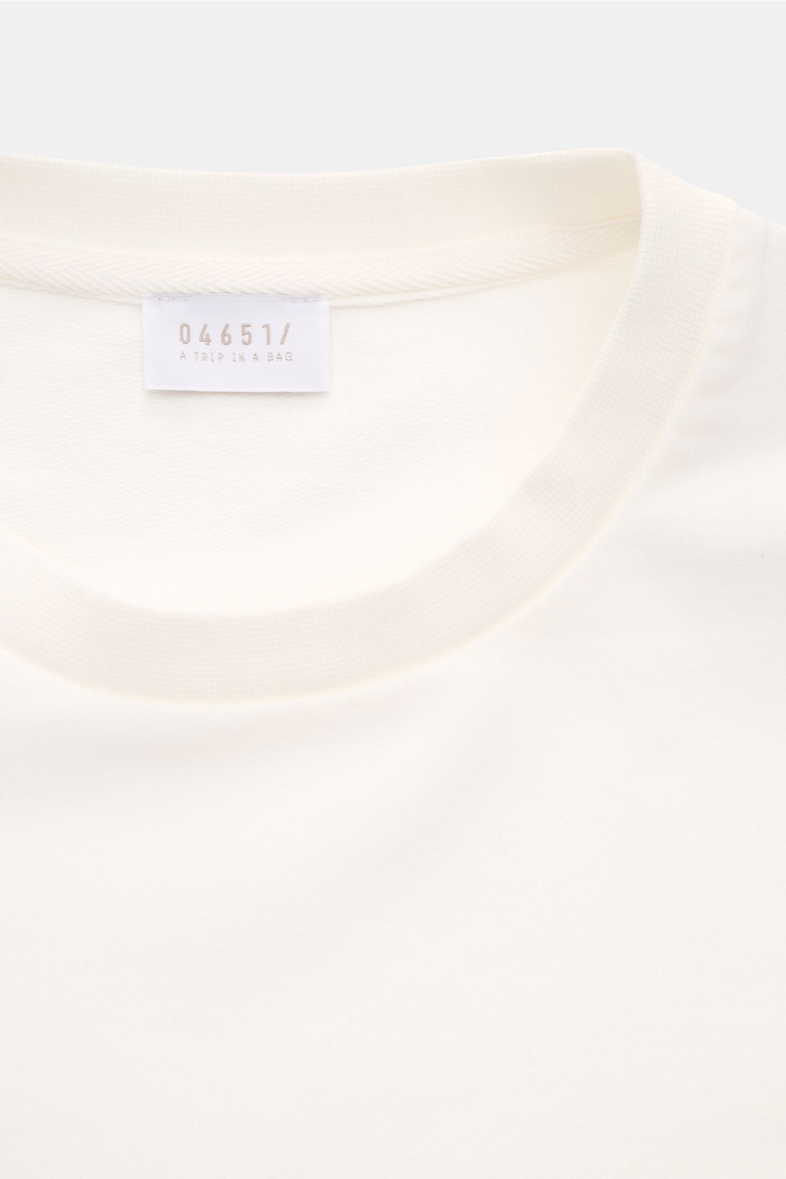 Close-up front view of the cream-colored neckline and label of the 04651/ A trip in a bag Crew neck T-shirt 'If Tee' cream. The uncomplicated cotton T-shirt 'IF Tee' by 04651/ A TRIP IN A BAG is a core basic for the new season that gives a taste of a rela