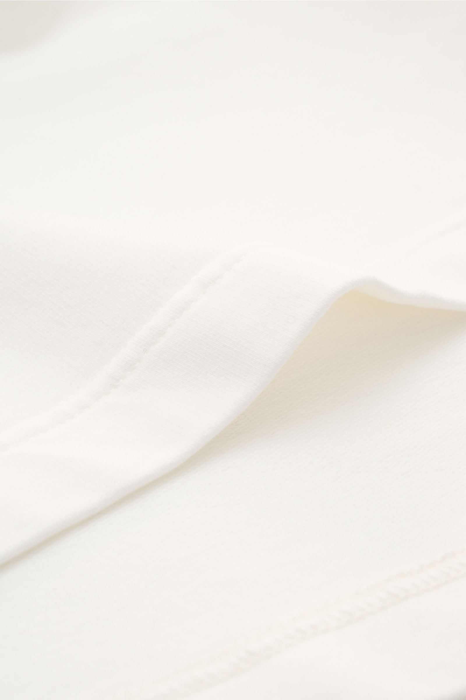 Close-up image of the cream fabric and seam of the 04651/ A trip in a bag Crew neck T-shirt 'If Tee' photographed from a side angle. The uncomplicated cotton T-shirt 'IF Tee' by 04651/ A TRIP IN A BAG is a core basic for the new season that give us a tast