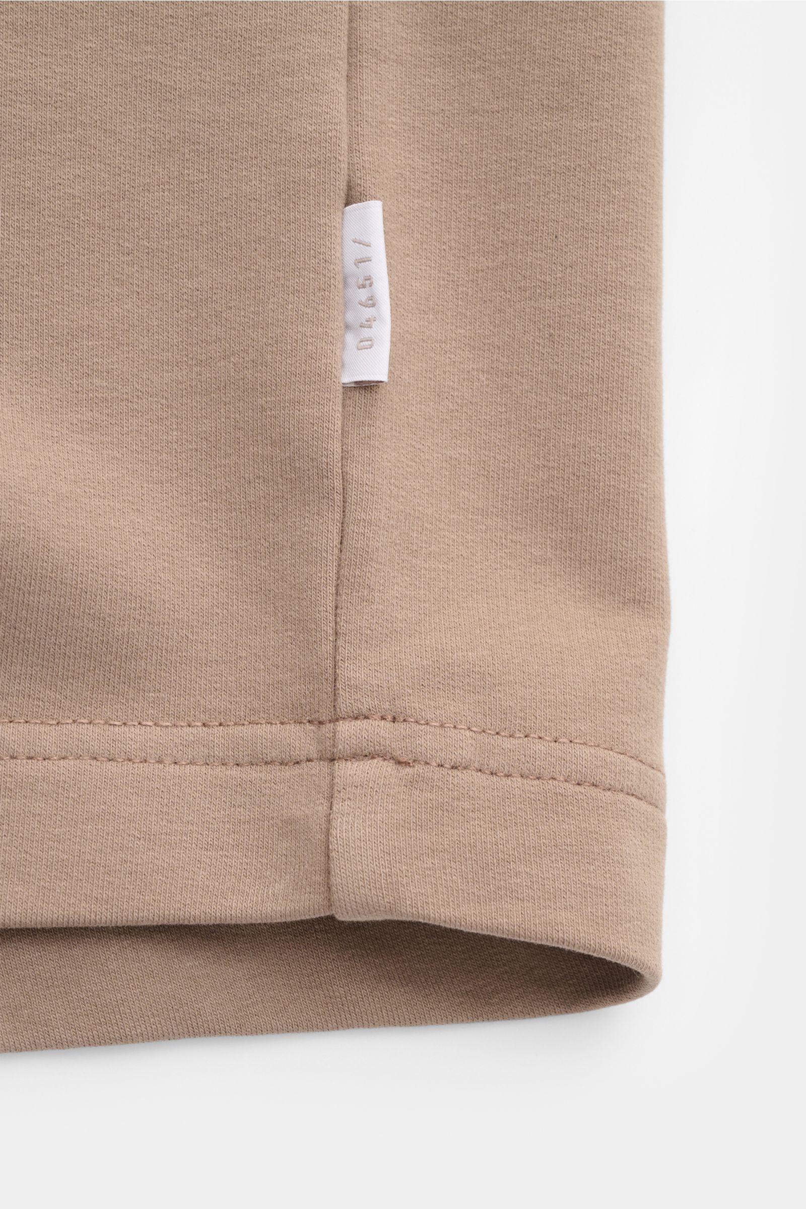 Close-up side seam of the 04651/ A trip in a bag Crew neck T-shirt 'If Tee' taupe showing a white woven label on taupe elasticated cotton fabric, photographed from a side angle.

The uncomplicated cotton T-shirt 'IF Tee' by 04651/ A TRIP IN A BAG is a 