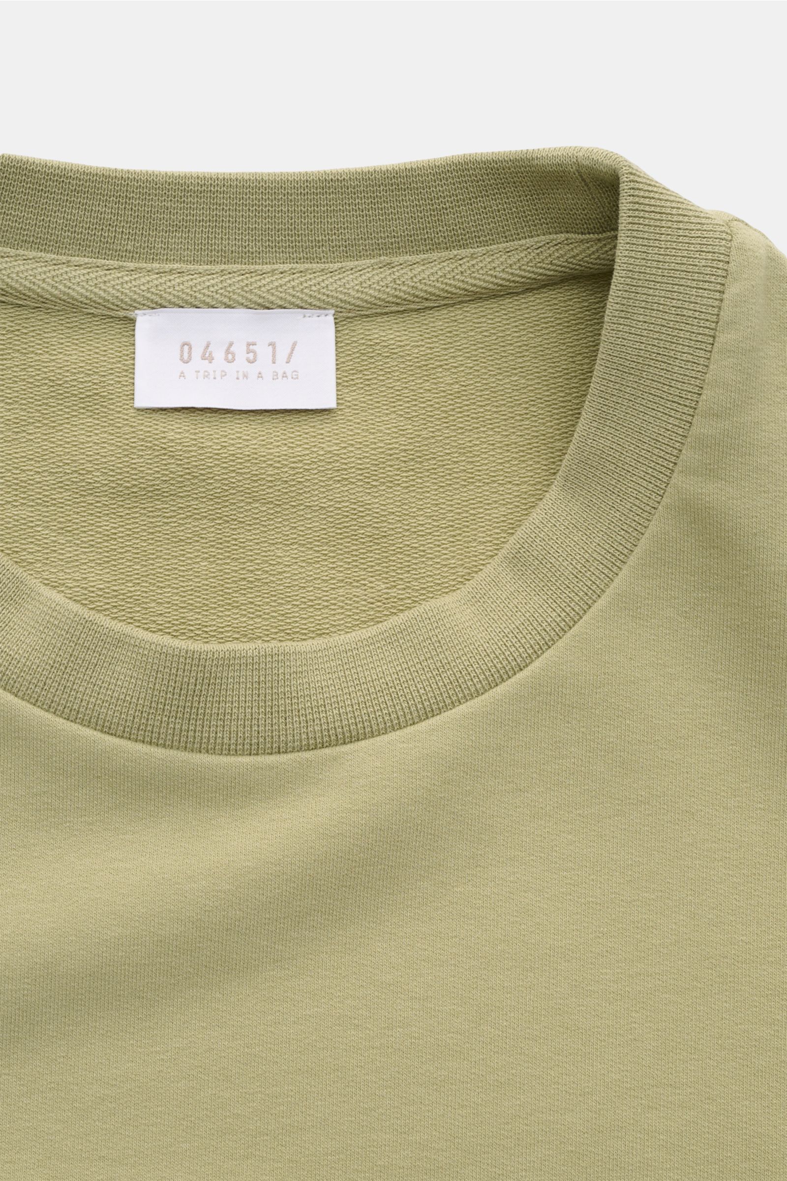 Close-up of the neckline and label of the 04651/ A trip in a bag Crew neck T-shirt 'If Tee' sage, photographed from above. The uncomplicated cotton T-shirt 'IF Tee' by 04651/ A TRIP IN A BAG is a core basic for the new season that give us a taste of a 