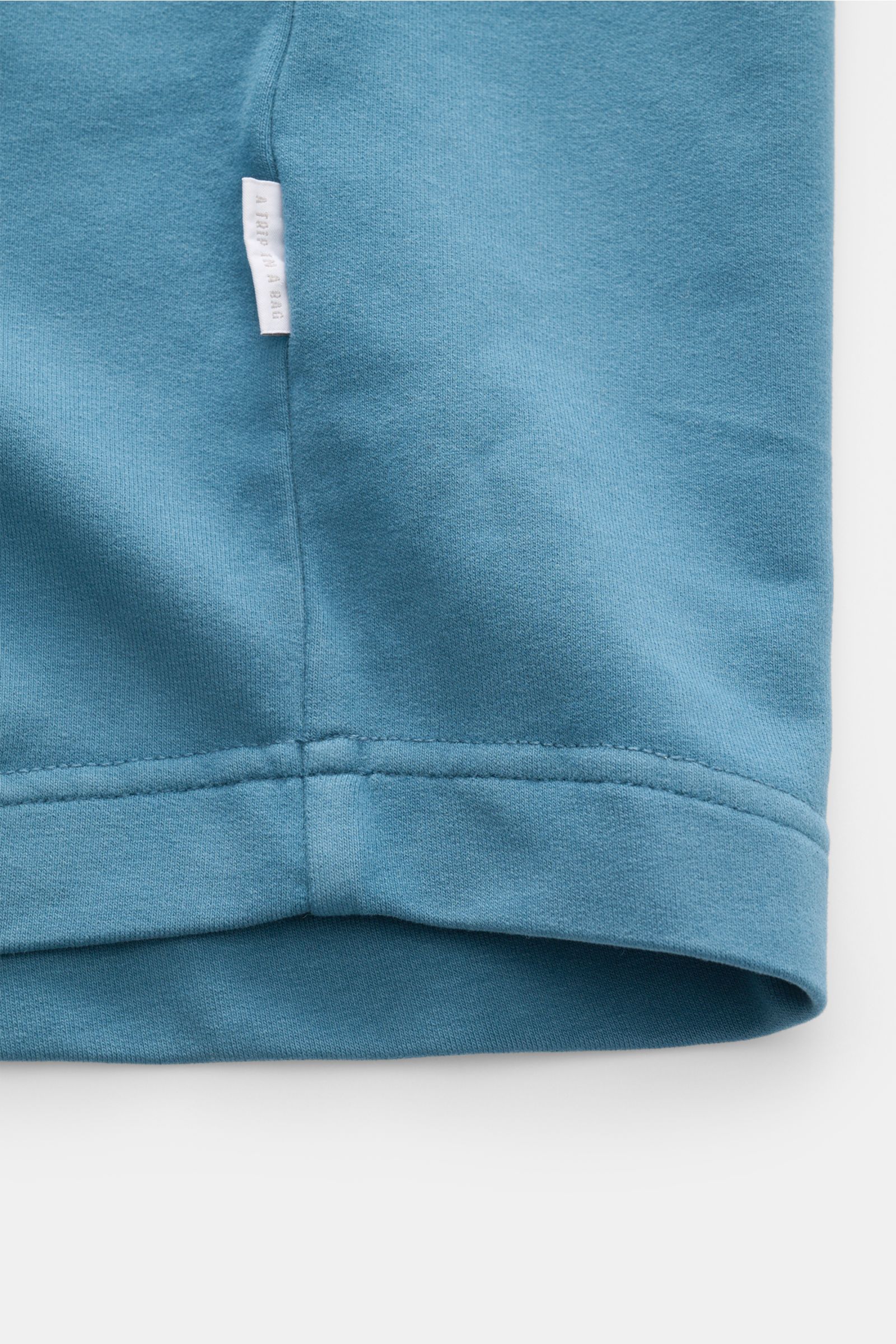 Close-up side view of the hem and side seam with woven label of the 04651/ A trip in a bag Crew neck T-shirt 'If Tee' teal cotton fabric.

The uncomplicated cotton T-shirt 'IF Tee' by 04651/ A TRIP IN A BAG is a core basic for the new season that give 