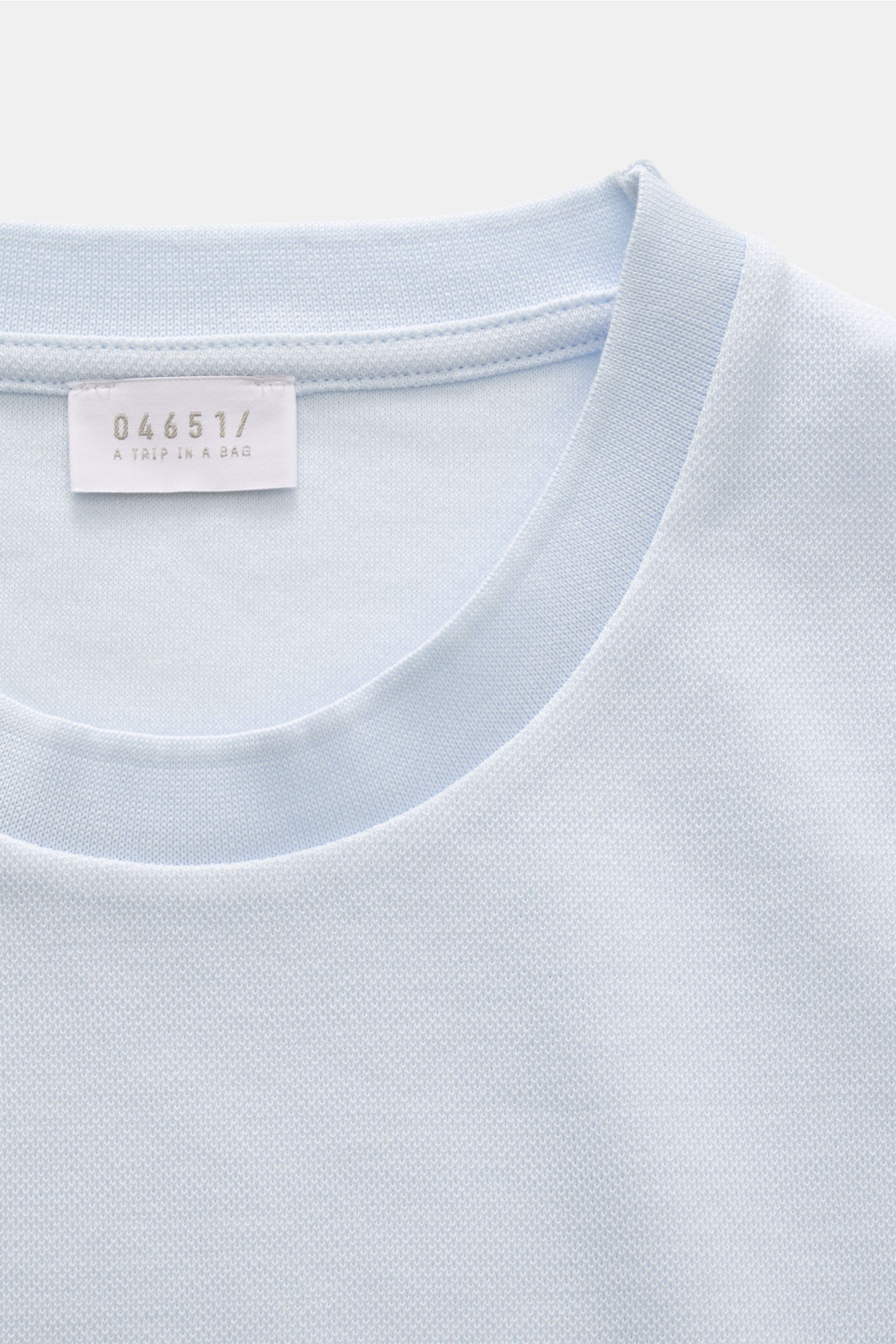 Frontnahes Detailfoto des pastellblauen 04651/ A trip in a bag Piqué-T-Shirts 'TP' mit Rundhalsausschnitt, Weblabel und Rippbündchen.