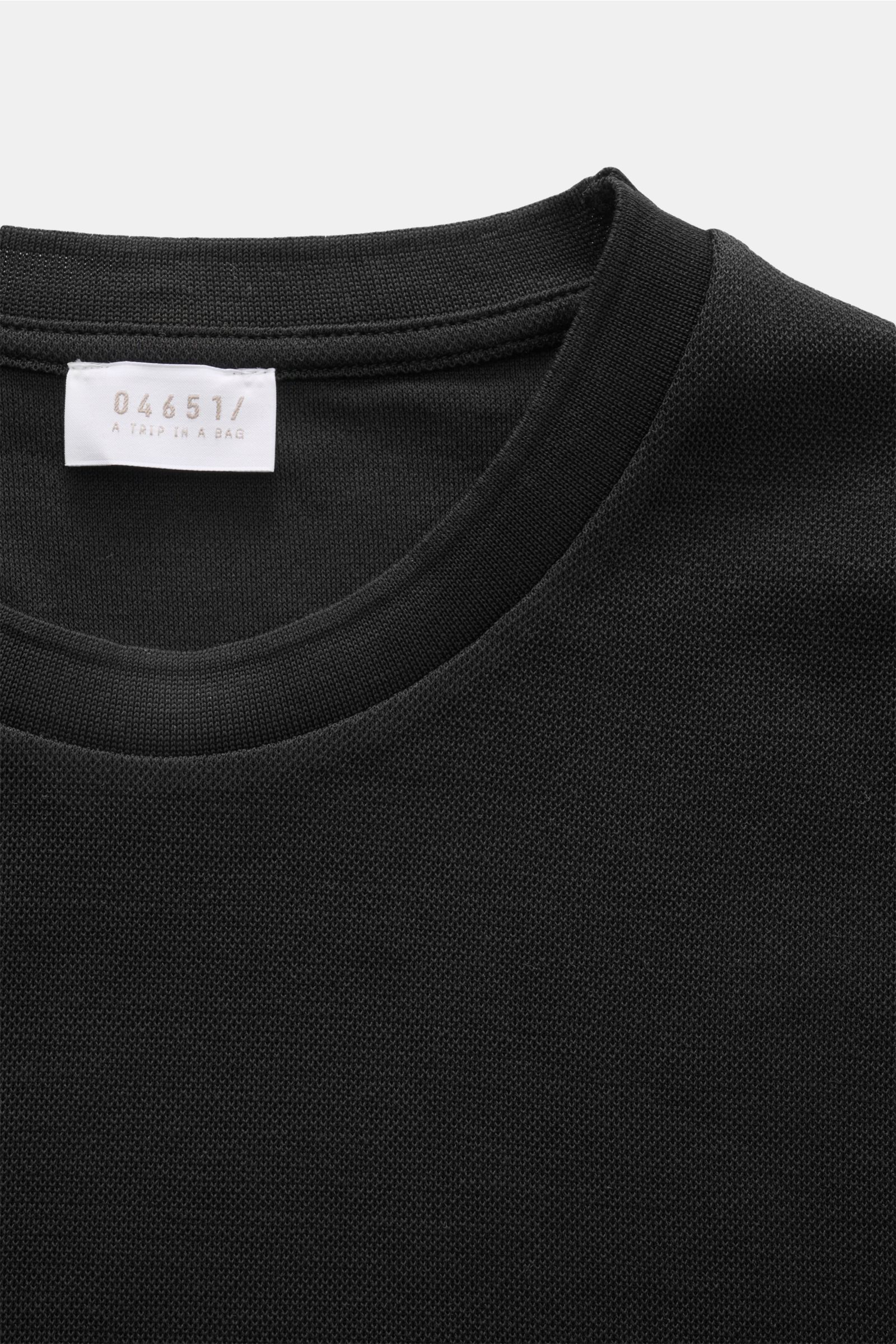 Nahaufnahme des Rundhalsausschnitts vom 04651/ A trip in a bag Piqué-T-Shirt 'TP' schwarz aus Piqué-Baumwolle mit Weblabel, Slim Fit und Rippbündchen.