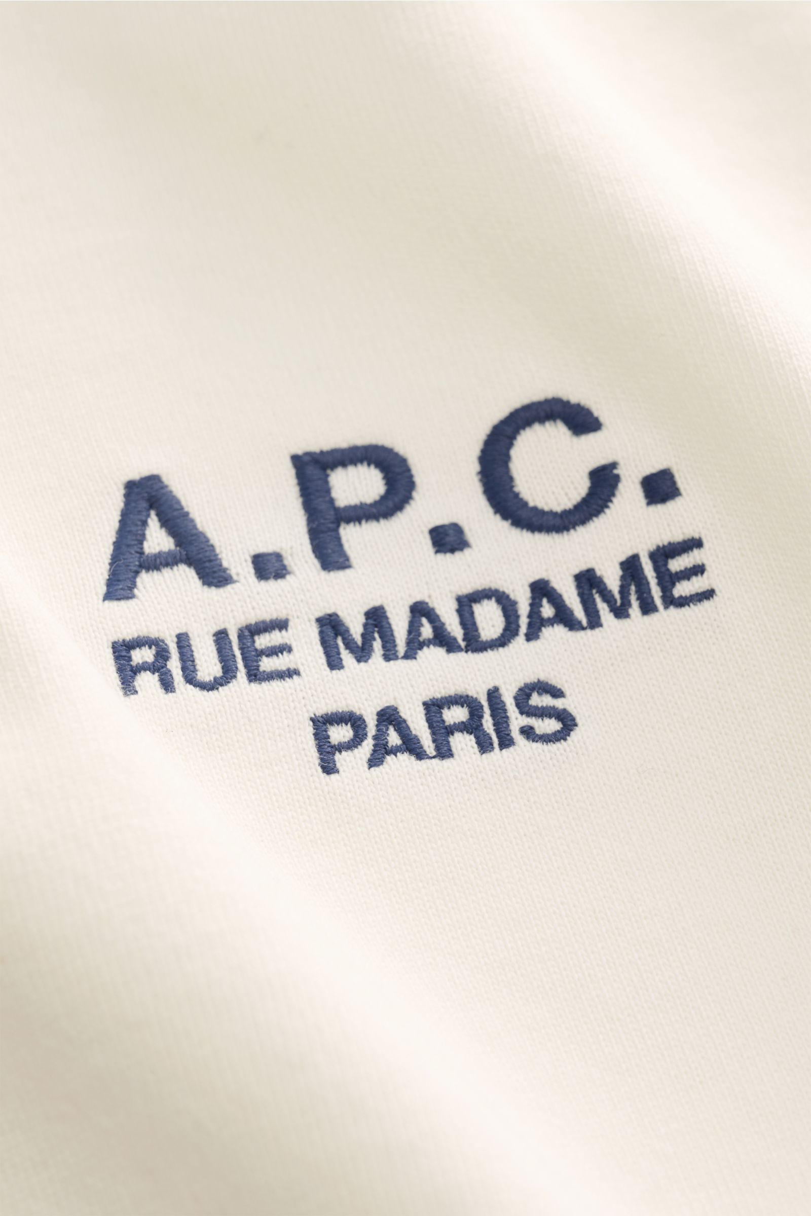 Nahaufnahme aus schräger Perspektive des A.P.C. Rundhals-T-Shirts 'Standard Rue Madame' offwhite mit weichem Baumwoll-Jersey und blauem Logo-Stitching.