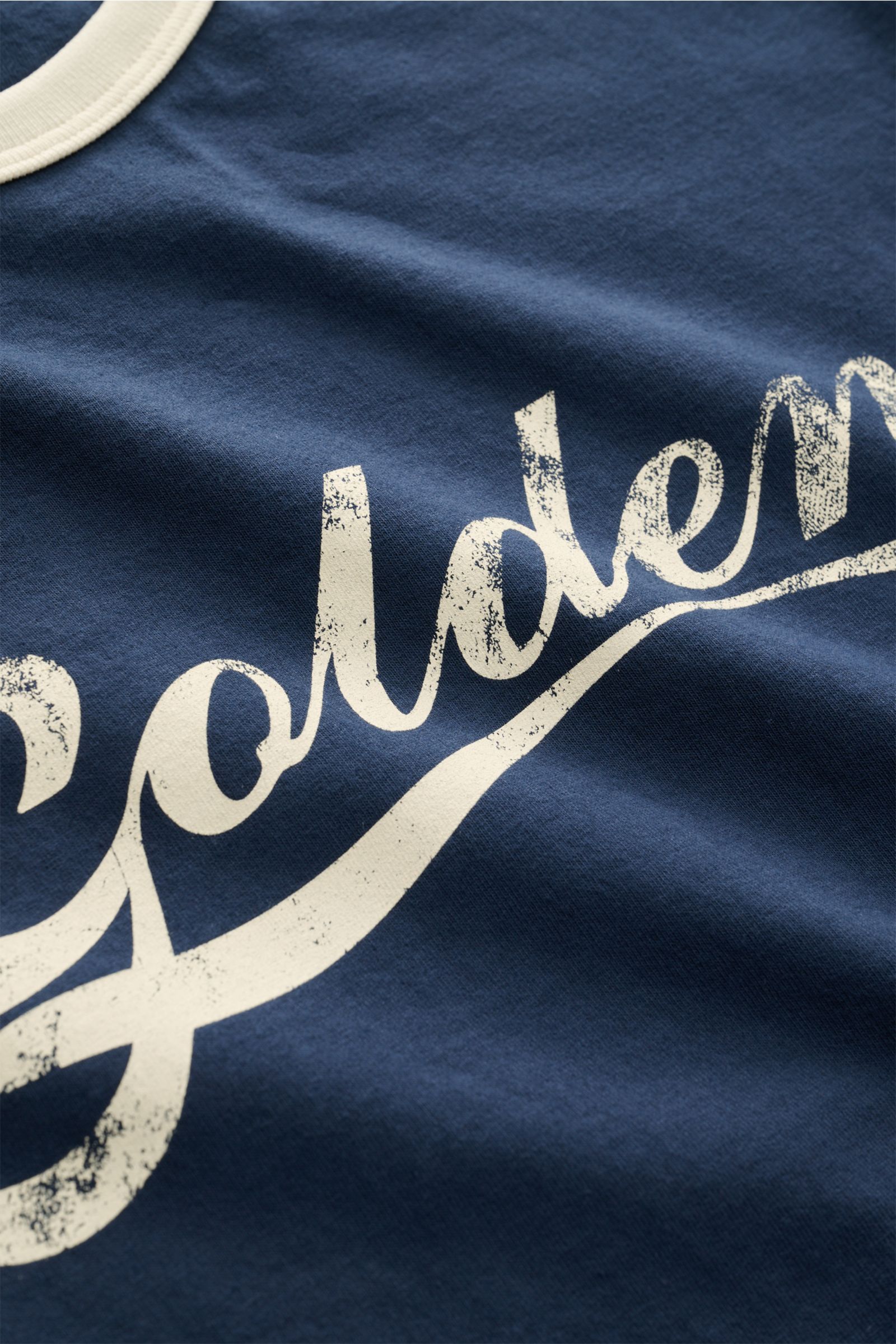 Close-up front view of Golden Goose Rundhals-T-Shirt navy/creme showing navy fabric with cream vintage-style script print and round neckline.

Retro-Sportswear neu interpretiert: Das T-Shirt von GOLDEN GOOSE sorgt mit markantem Print für legere Sommerl