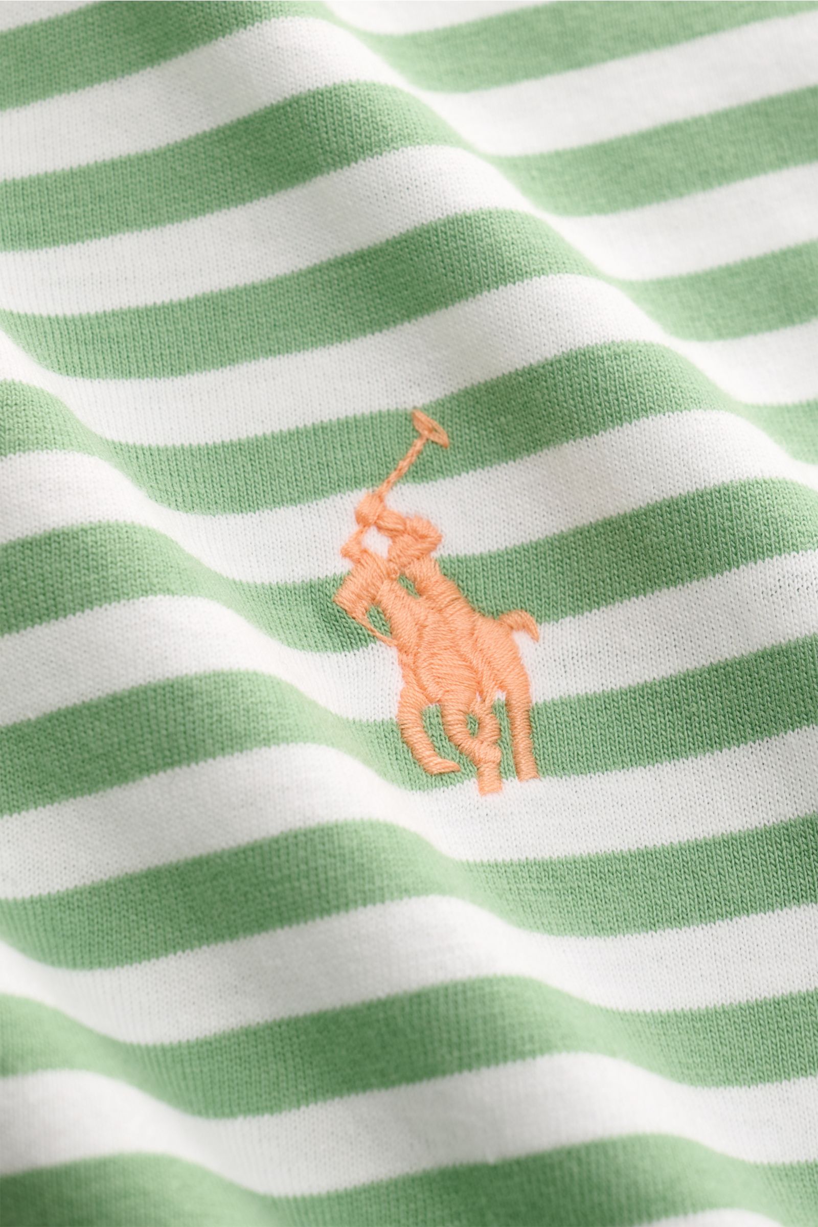 Nahaufnahme des Polo Ralph Lauren Rundhals-T-Shirts grünweiß gestreift mit weichem Baumwoll-Jersey, Slim Fit und orangefarbenem Logo-Stitching auf der Brust, fotografiert aus leicht seitlicher Perspektive.