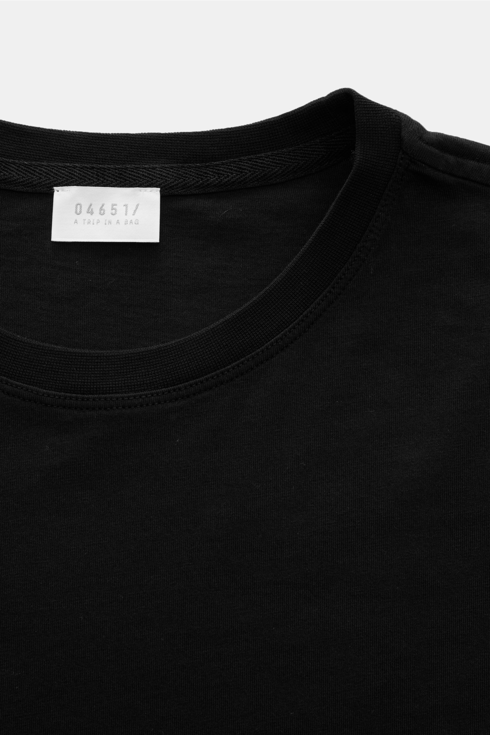 Close-up front view of the neckline of the 04651/ A trip in a bag Long sleeve black, jersey made of pure cotton, soft feel, regular fit, crew neck, with a small woven label inside the collar.