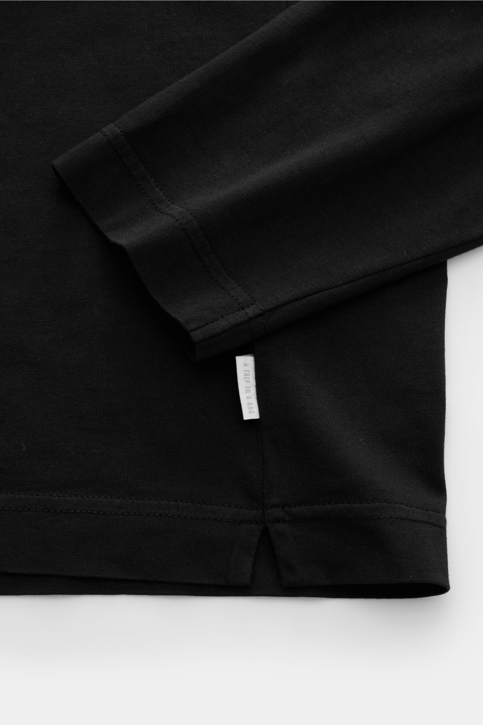 Close-up view of the hem and sleeve of the 04651/ A trip in a bag Long sleeve black, showing jersey made of pure cotton, soft feel, regular fit, crew neck, and small woven label.