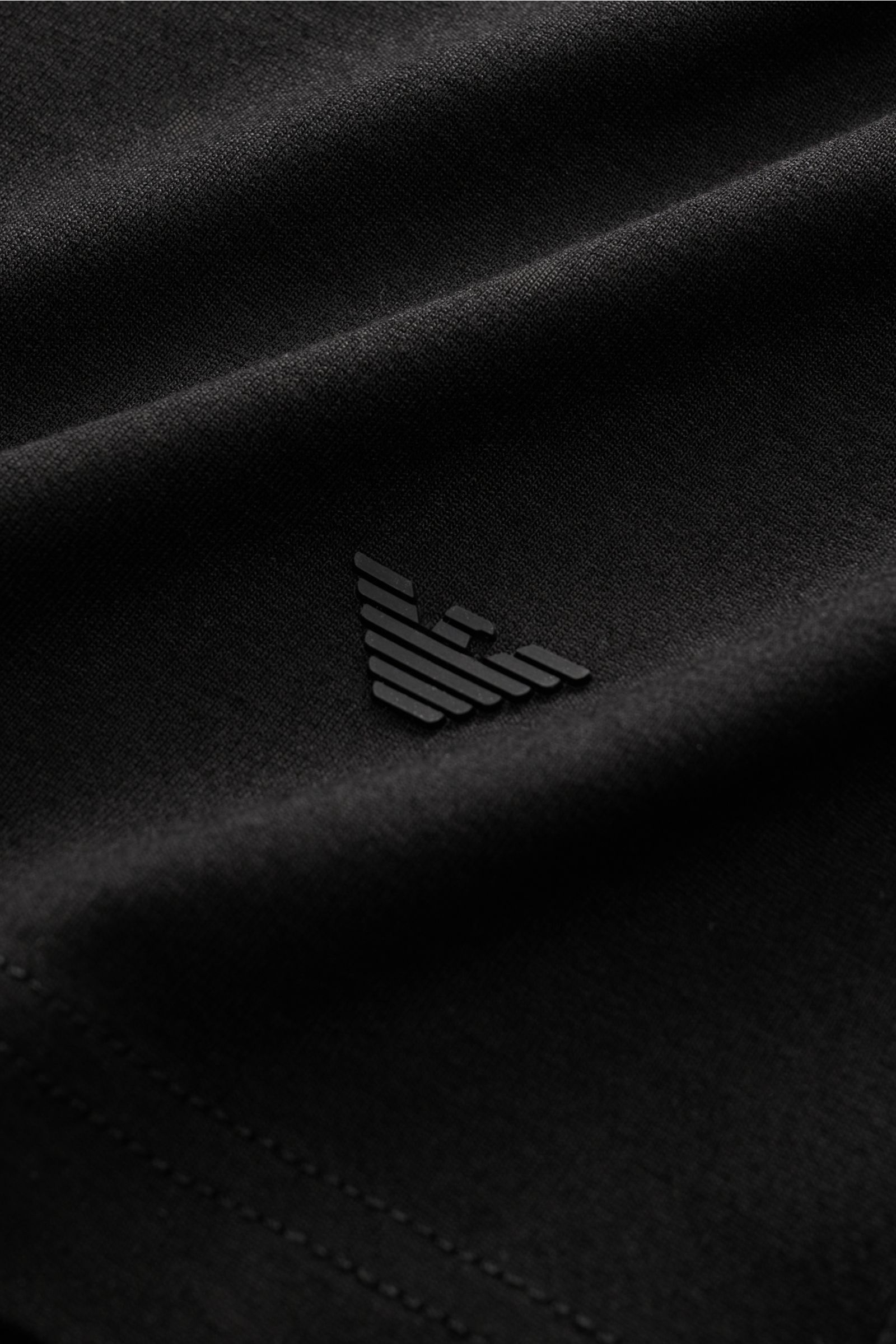 Nahaufnahme des Emporio Armani Rundhals-T-Shirts schwarz, Detail des gummierten Logos am Saum aus elastischer Viskose mit feinem Jersey.