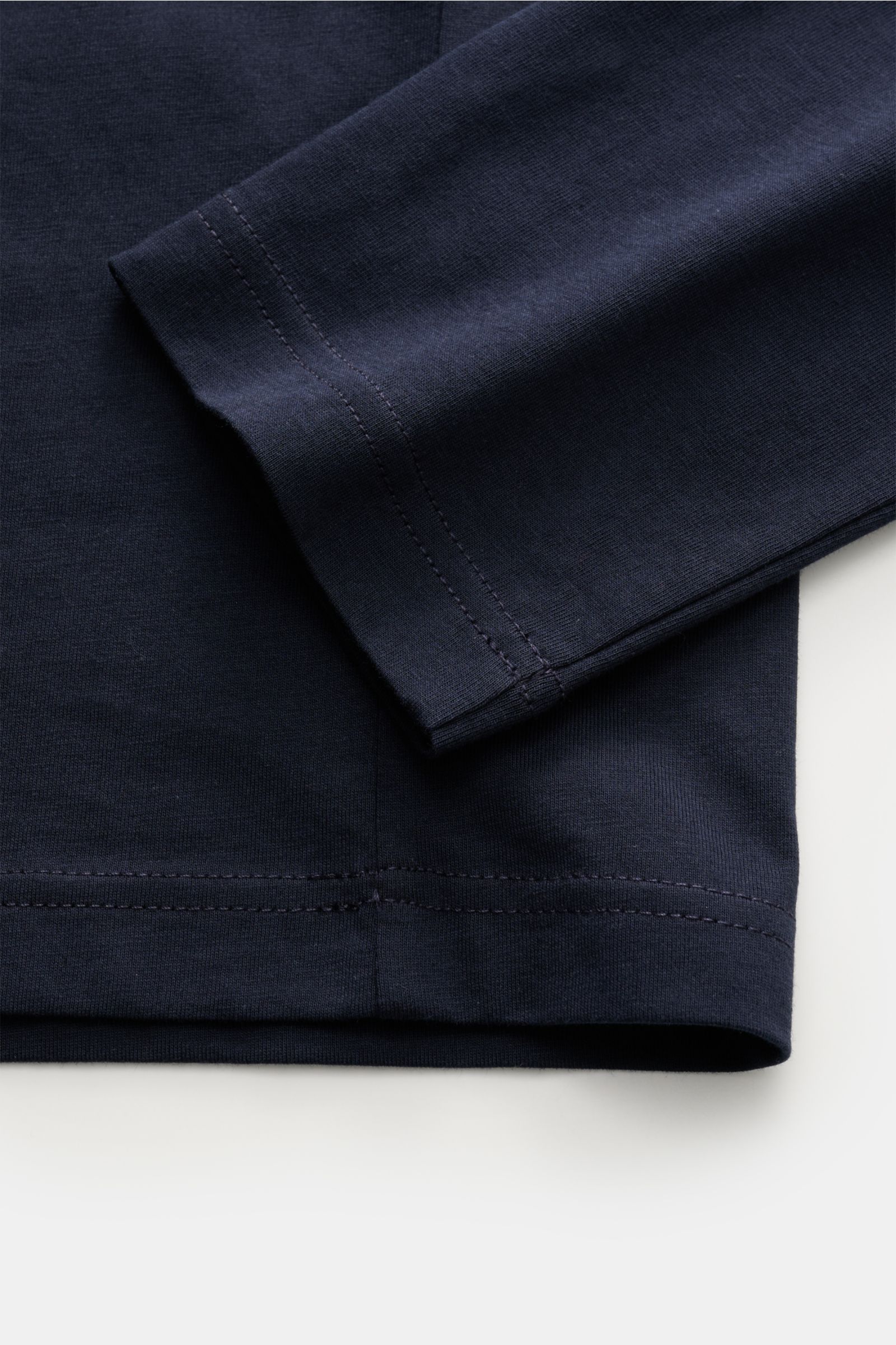 Nahaufnahme des navyfarbenen Belstaff Rundhals-Longsleeve aus leichtem Baumwolljersey, Slim Fit, mit Rundhalsausschnitt und BELSTAFF-Weblabel auf der Brust, fotografiert von unten seitlich.