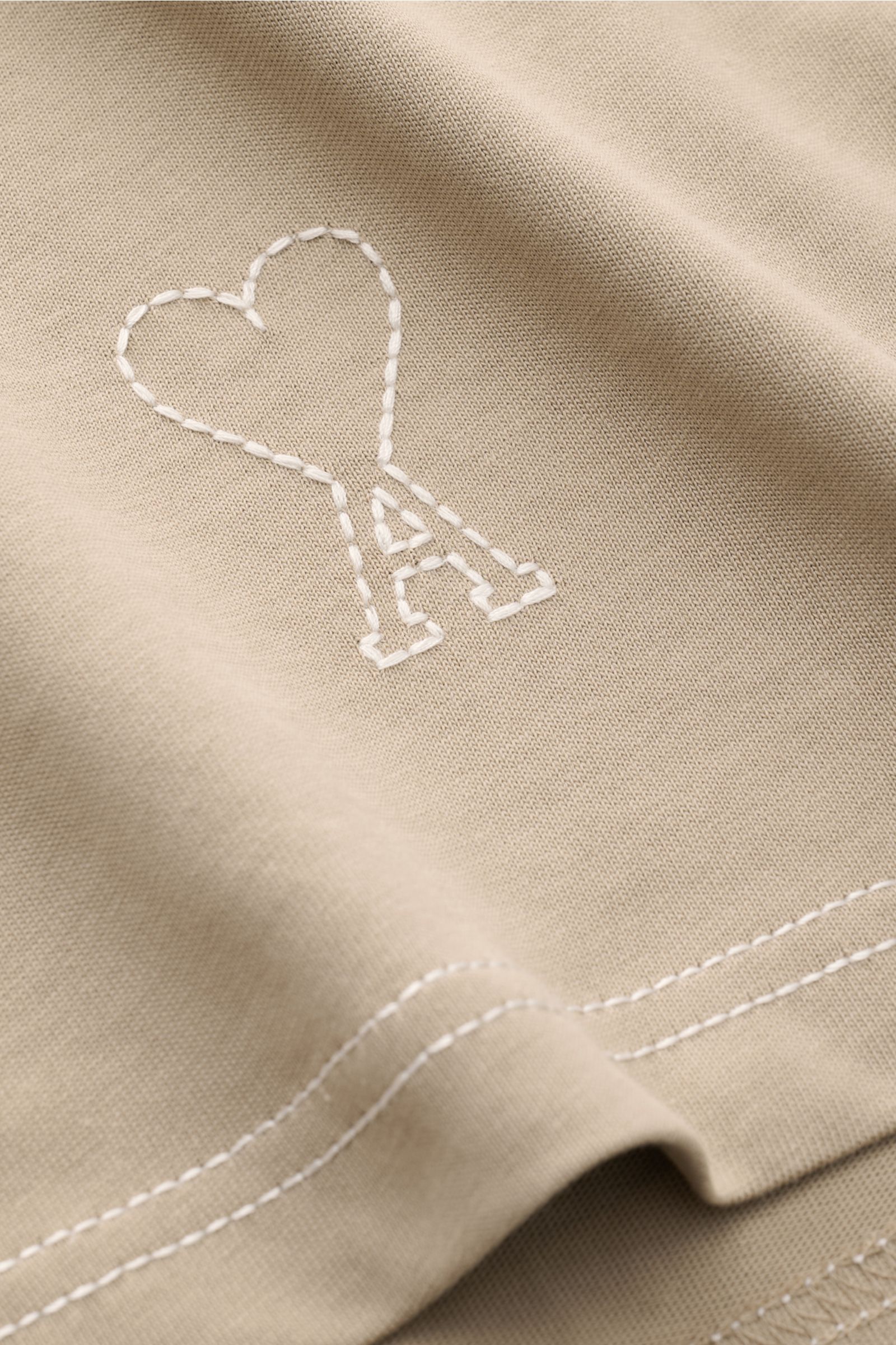 Close-up front view of Ami Paris Long sleeve taupe showing quilted heart logo and detailed stitching on taupe cotton fabric.

Create perfect urban looks with this long sleeve by AMI PARIS – the quilted seams and signature heart logo on the hem make it 