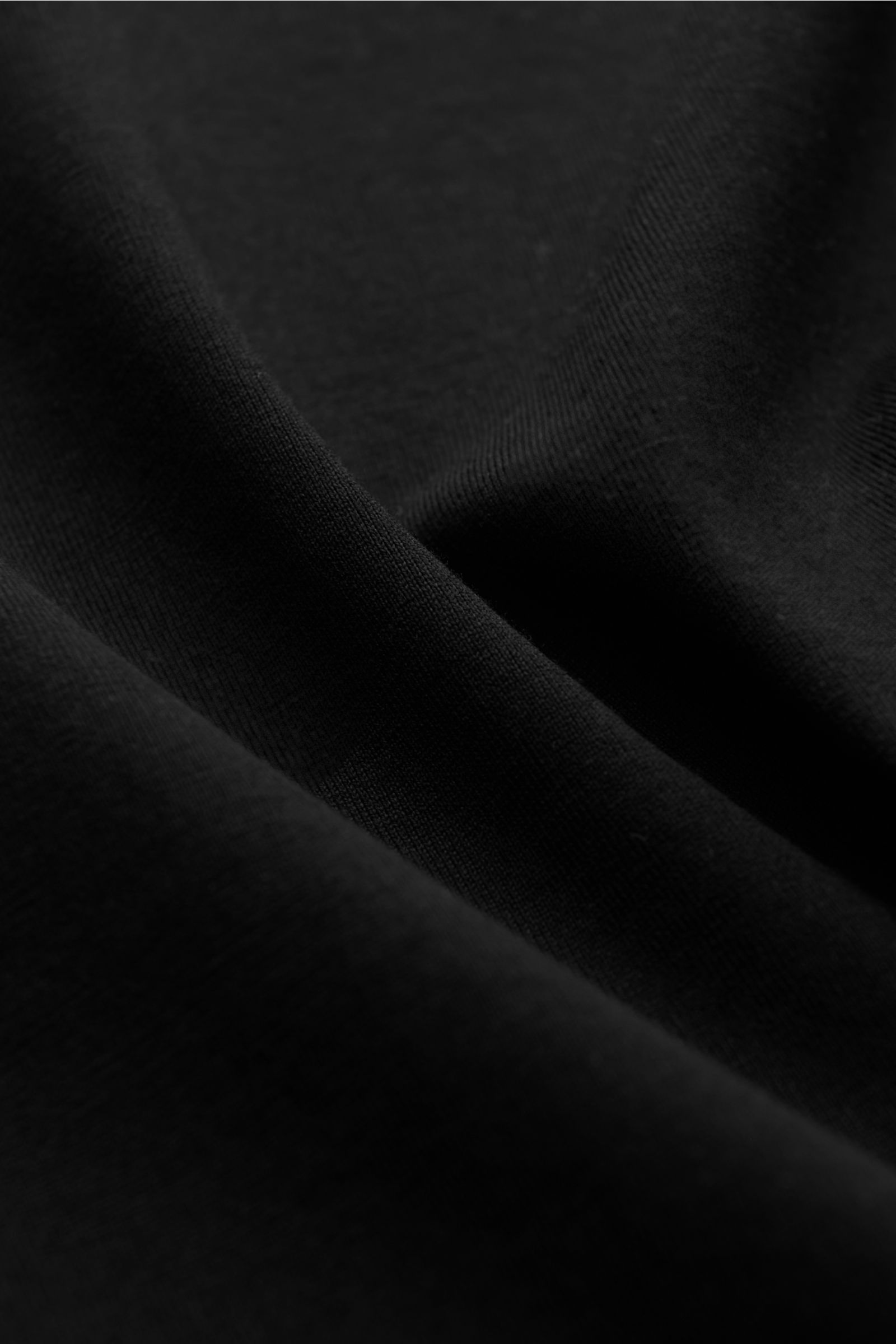 Close-up view of black fabric texture showing fine jersey knit of Stefan Brandt Rundhals-Longsleeve 'Eli' schwarz. Die Jersey-Essentials von STEFAN BRANDT punkten mit der exklusiven Verarbeitung hochwertiger organischer Pima-Baumwolle: farbecht, formstabi