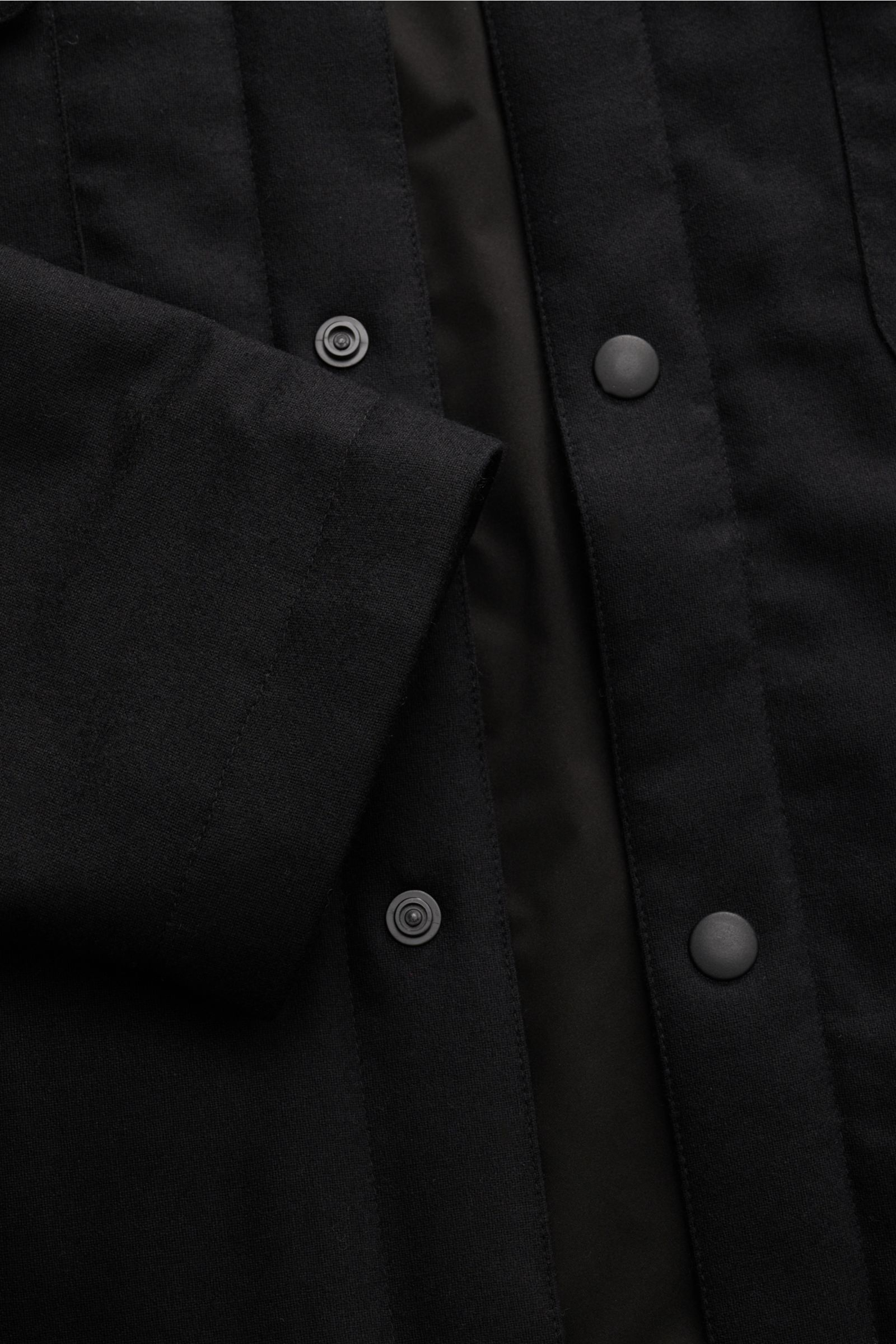 Close-up shot from above of the 04651/ A trip in a bag Reversible overshirt black showing snap button placket, soft wool, cashmere, microfibre blend, slight stretch, lightweight padding, tonal lining, and smooth fabric texture.