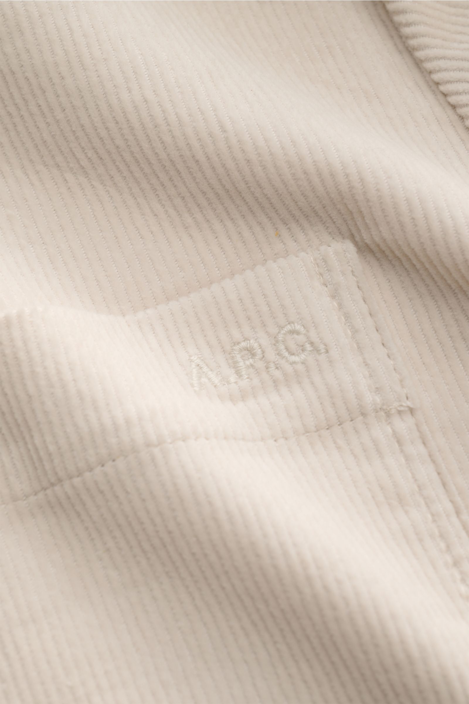 Close-up front view of the creamy corduroy fabric and tonal logo stitching on the A.P.C. Overshirt 'Leon' creme, made of pure cotton with a soft touch. Das klassische Overshirt aus feinem Baumwoll-Cord von A.P.C. ist das perfekte Layering-Piece für den
