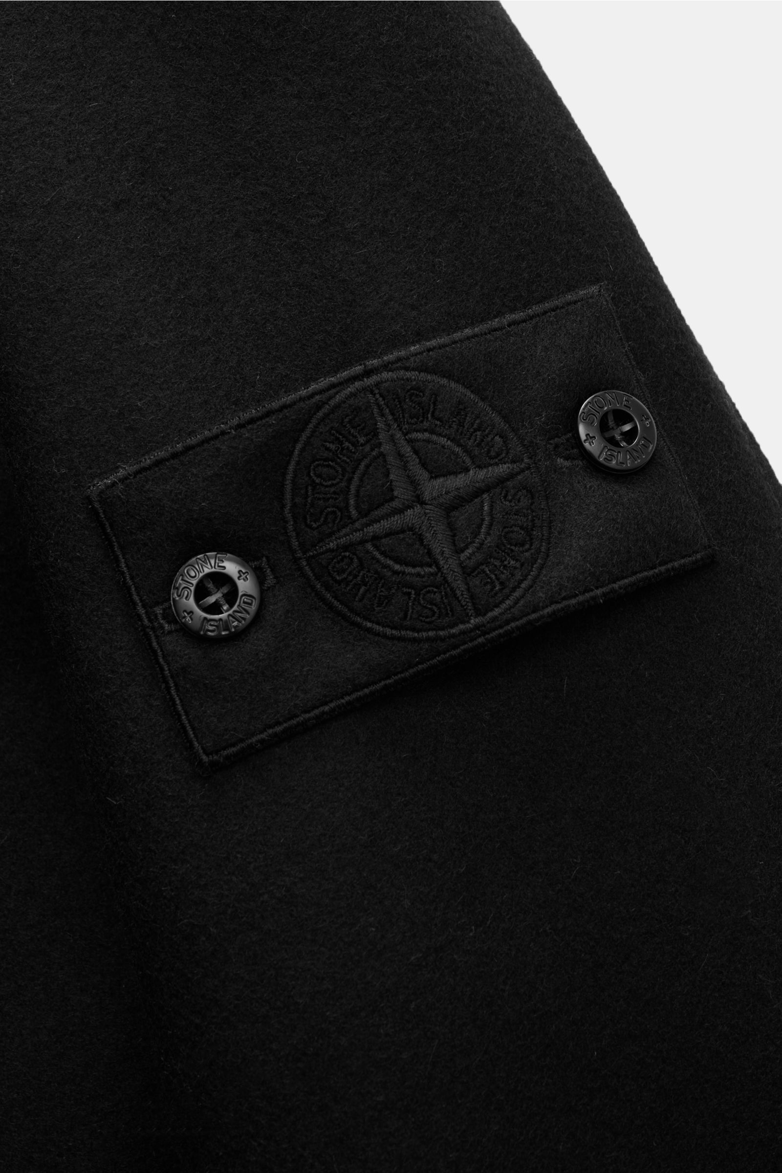 Schwarz gefilztes Stone Island Overshirt 'Ghost Piece' aus Woll-Mix, Nahaufnahme des monochromen Logo-Badges in seitlicher Perspektive.