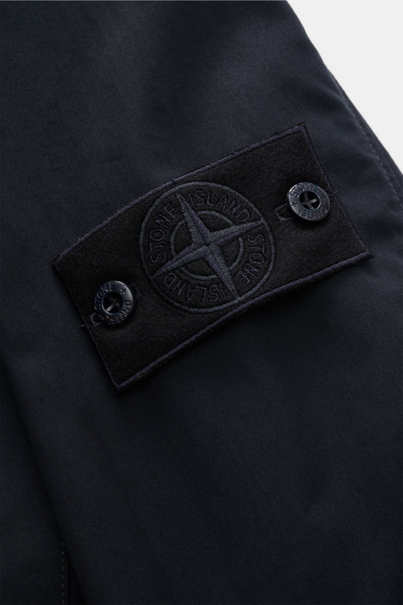 Close-up detail of the tonal logo badge on the sleeve of the Stone Island Overshirt 'Weather Proof Cotton Canvas Ghost Piece' navy, photographed from a top-down perspective.

Description: Get the best casual look for autumn with the overshirt 'Weather 