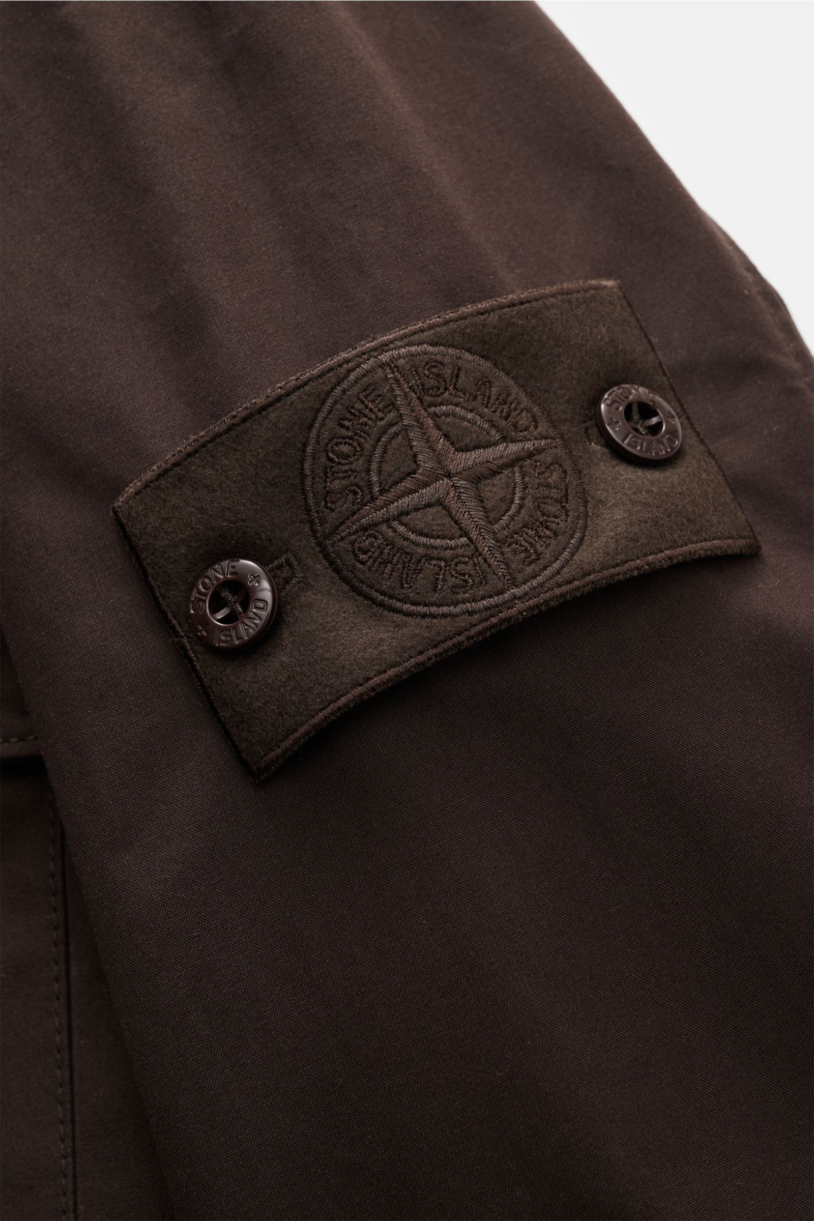 Nahaufnahme des tonalen Kompass-Logos am Ärmel des Stone Island Overshirts 'Weather Proof Cotton Canvas Ghost Piece' dunkelbraun aus Baumwoll-Canvas, wind- und wasserabweisend.