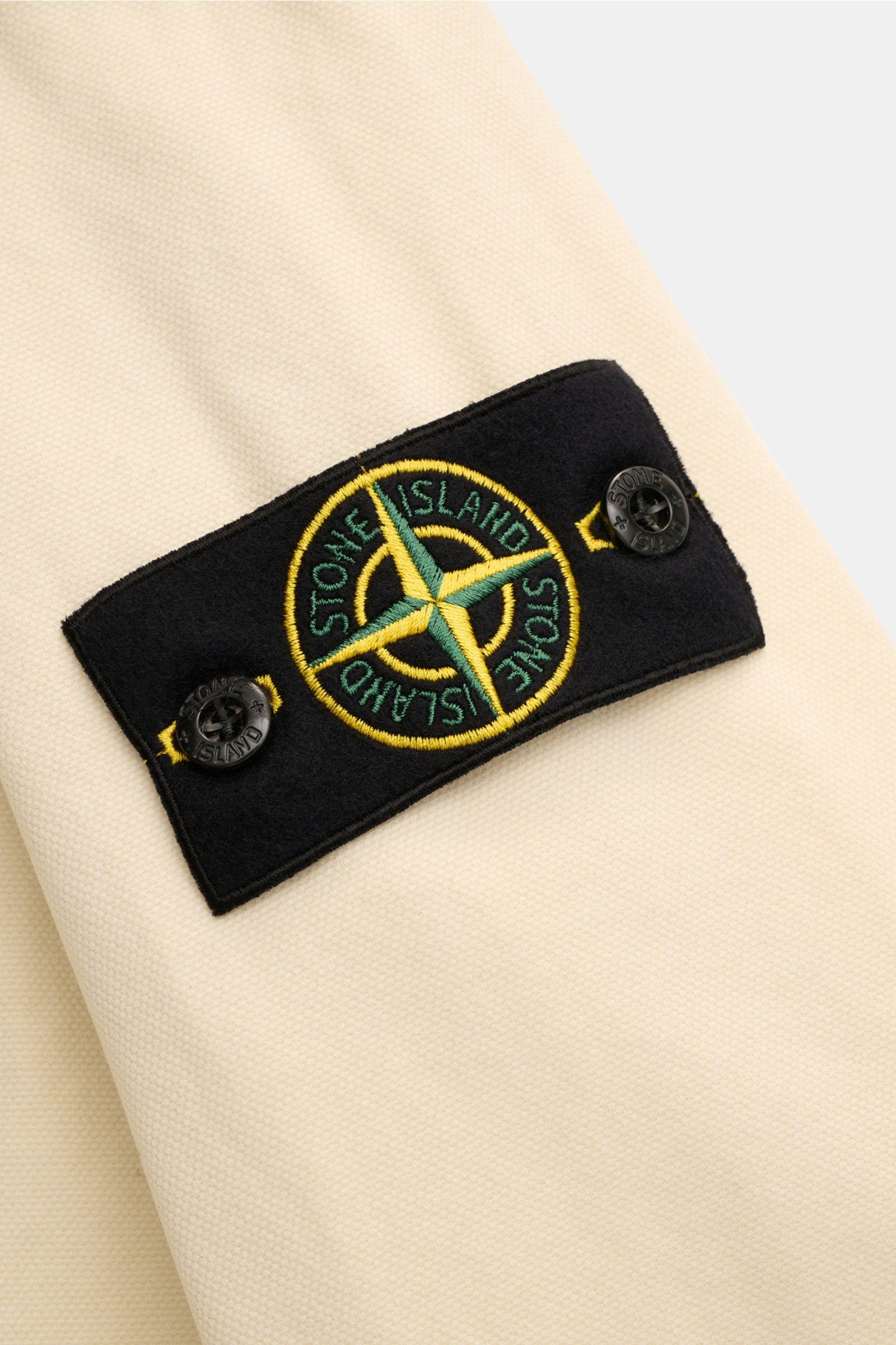 Alt-Tag (124 Zeichen):
Nahaufnahme des Kompass-Badges am Ärmel des Stone Island Overshirt 'Organic Panama' creme aus reiner Baumwolle, weicher Griff.