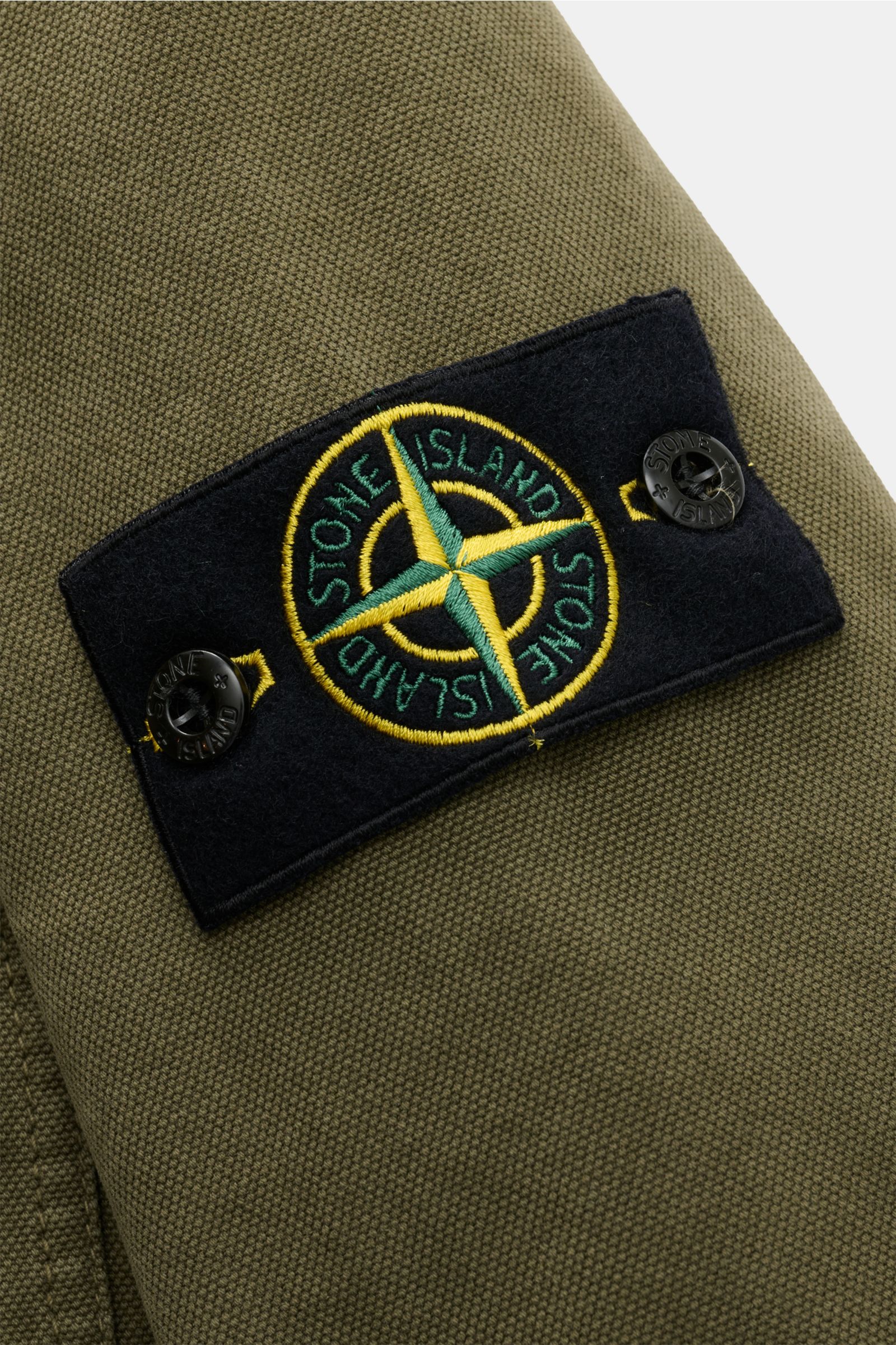 Stone Island Overshirt 'Organic Panama' oliv in Nahaufnahme, Detail des Kompass-Badges auf dem Ärmel aus reiner Baumwolle.