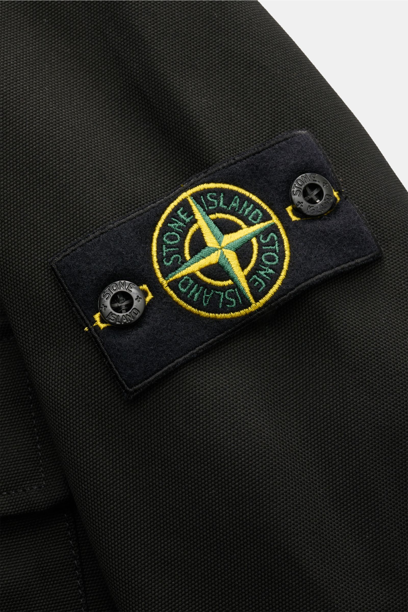Close-up view of the Stone Island Overshirt 'Panama Cotton' schwarz showing the black cotton canvas fabric and the typical compass badge on the sleeve. Robustes Overshirt: Dieser Hybrid in typischer STONE ISLAND-Manier ist aus Baumwoll-Canvas gefertigt un