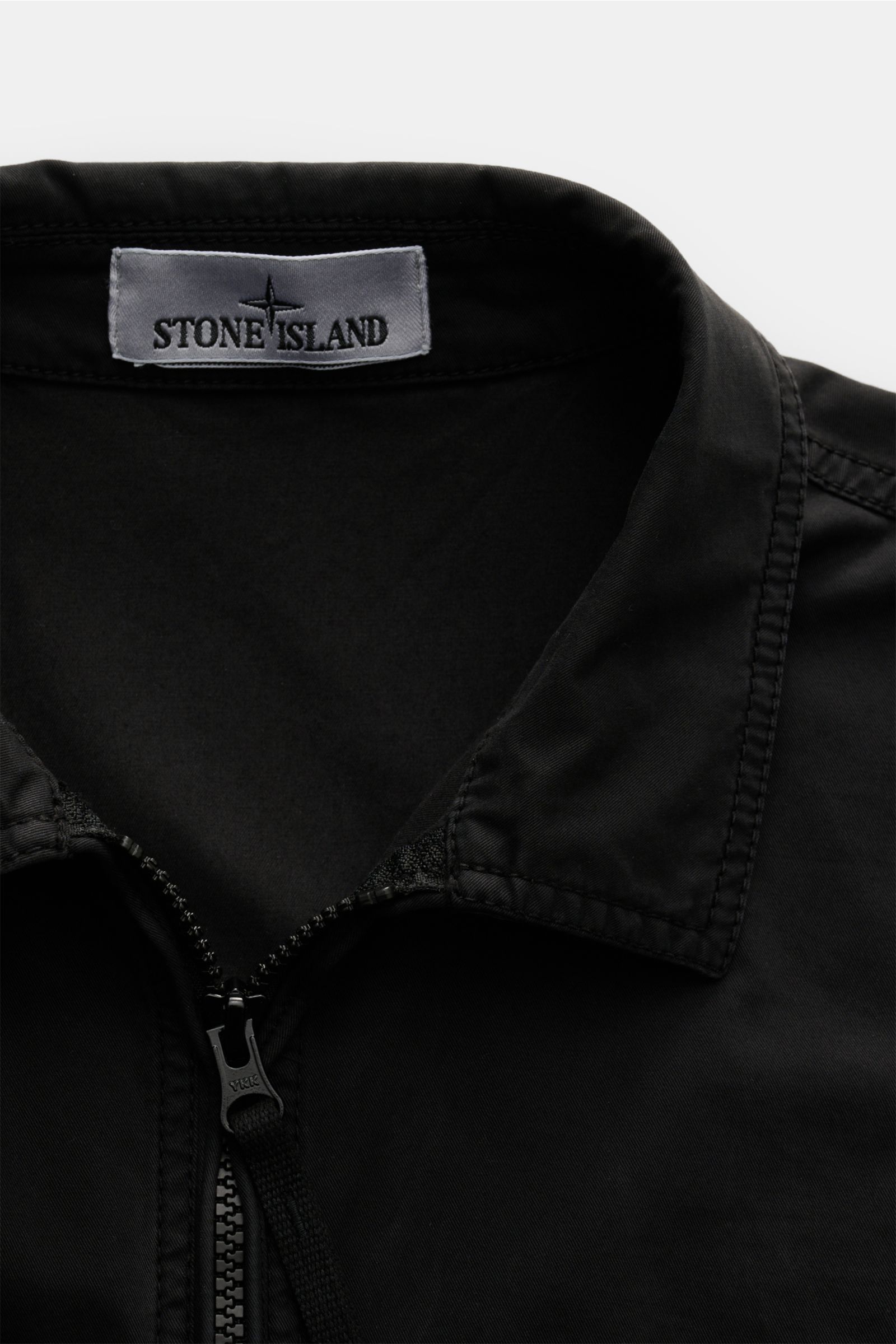 Close-up front view of the Stone Island Overshirt schwarz showing the collar, zipper, and label, made of twill aus reiner Baumwolle, elastische Qualität, weicher Griff, sehr leichte Qualität, garment dyed, Slim Fit, Zwei-Wege-Reißverschluss, Umlegekragen,