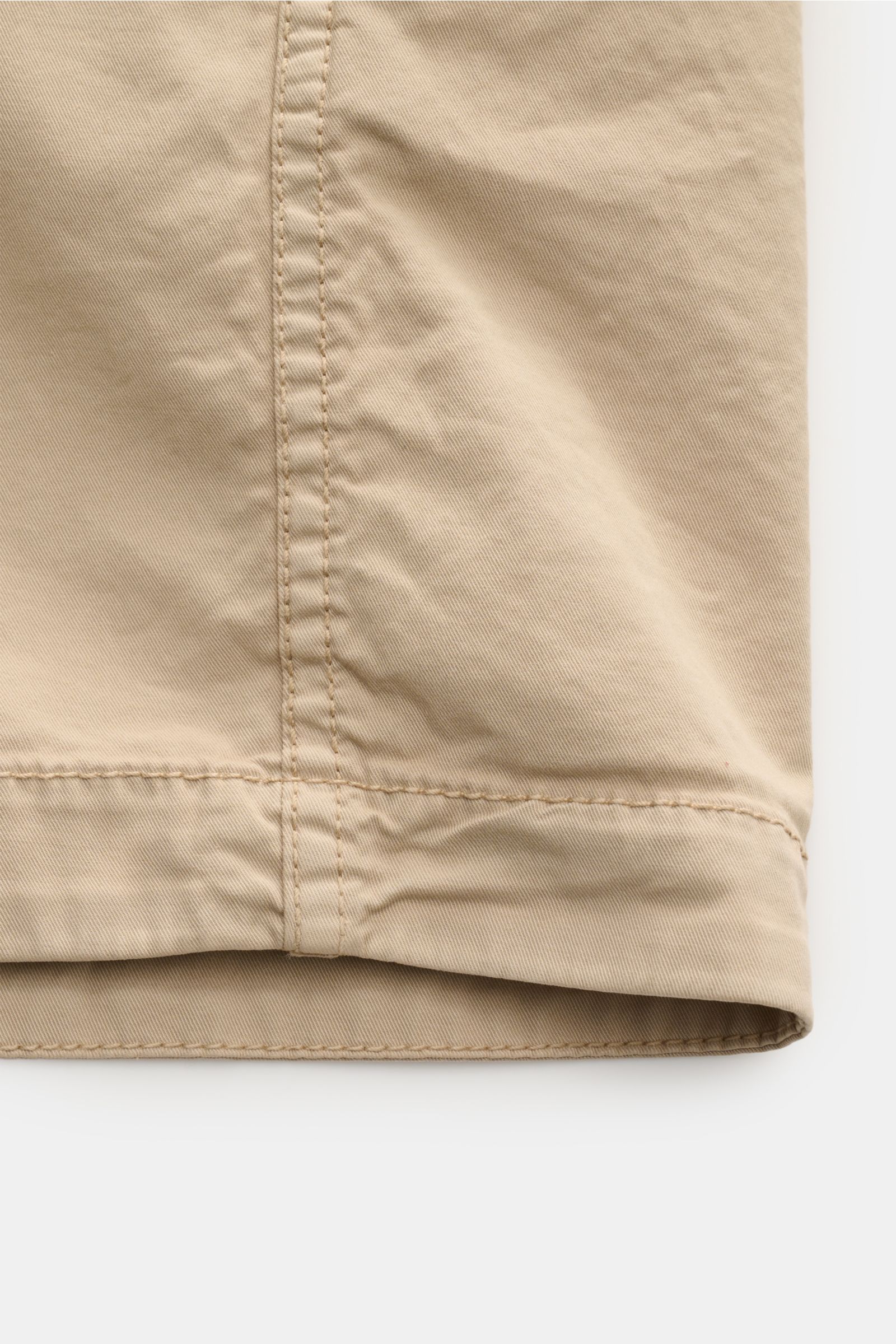 Stone Island Overshirt beige aus twill Baumwolle, elastisch, weich, leicht, garment dyed, Slim Fit, Zwei-Wege-Reißverschluss, Umlegekragen, Brusttasche mit Zipper, Kompass-Badge am Ärmel, regulierbare Ärmelabschlüsse, Detailaufnahme des Saums von unten.