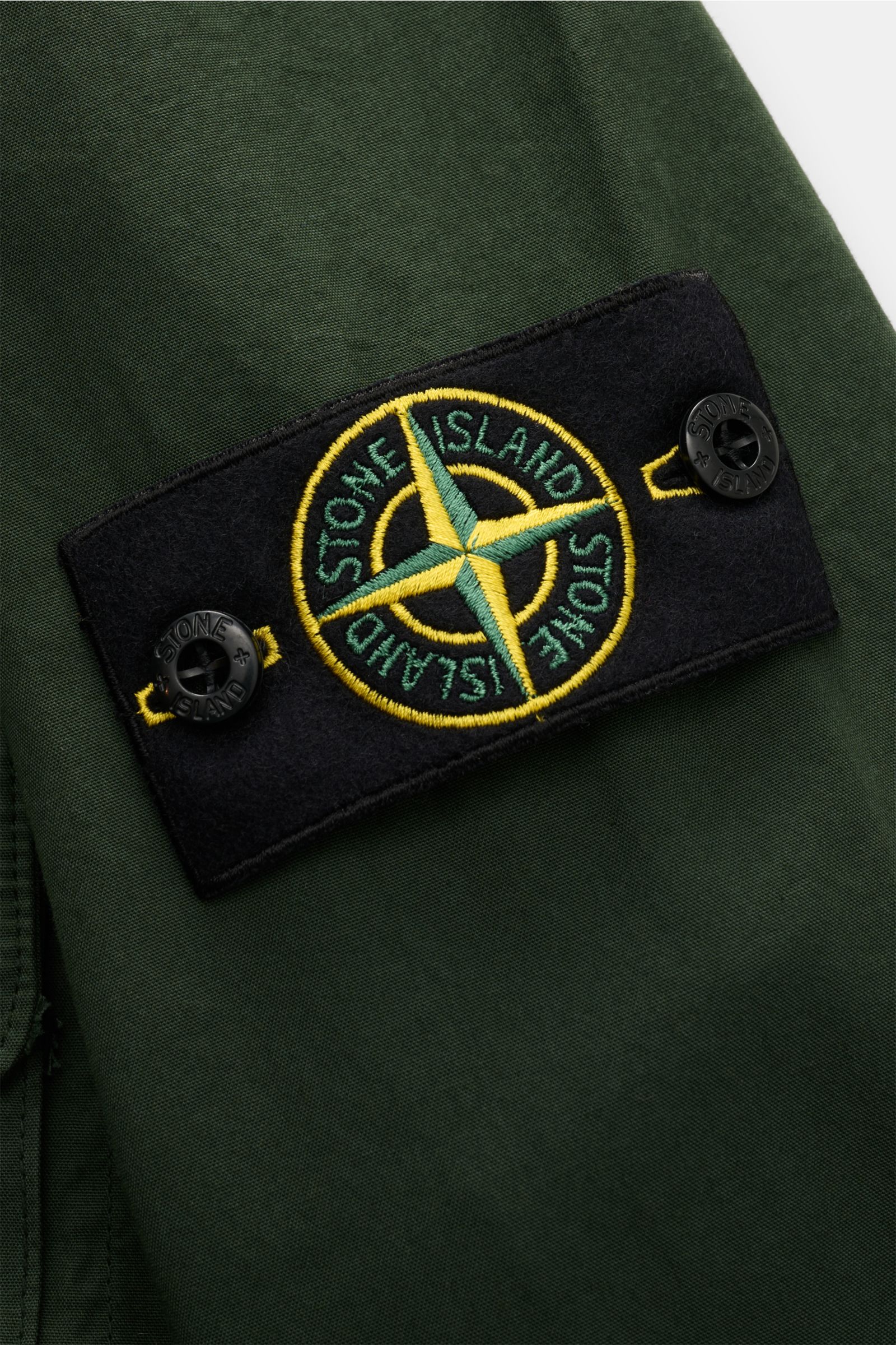 Stone Island Overshirt 'Canvas Weave' dunkelgrün, Detailansicht Ärmel mit typischem Kompass-Badge, Canvas Baumwolle, Slim Fit, robuste Qualität, Zwei-Wege-Reißverschluss, Umlegekragen, Brusttasche mit Zipper und Knopf, Ärmel mit Druckknopf, ungefüttert.