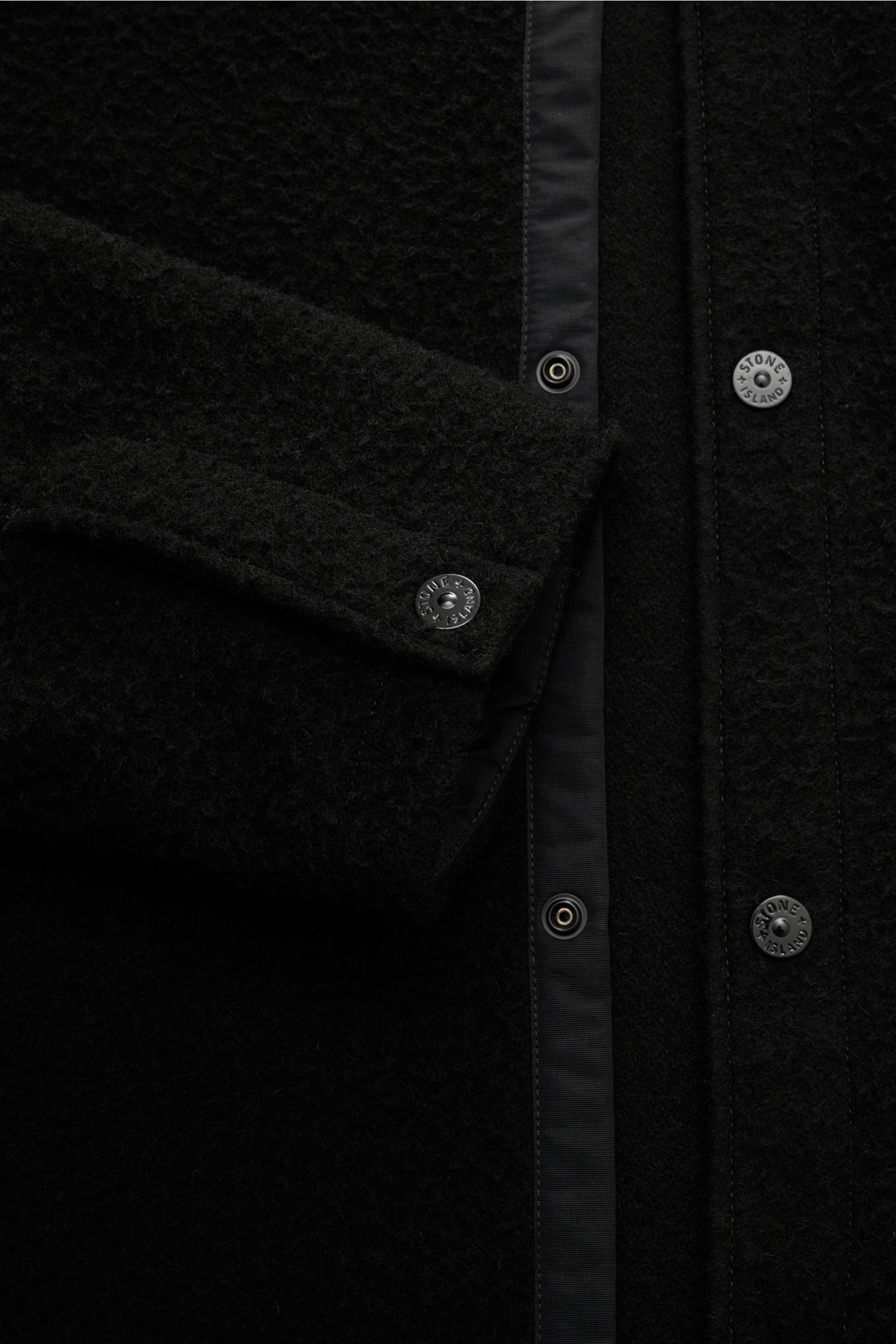 Nahaufnahme der Stone Island Jacke 'Panno Ratinato' schwarz aus Slim Fit mit Druckknopfleiste, Umlegekragen, Kompass-Badge, Woll-Microfaser-Mix, strukturierter Haptik, Druckknopf-Ärmelabschlüssen und regulierbarer Saumweite, frontal fotografiert.