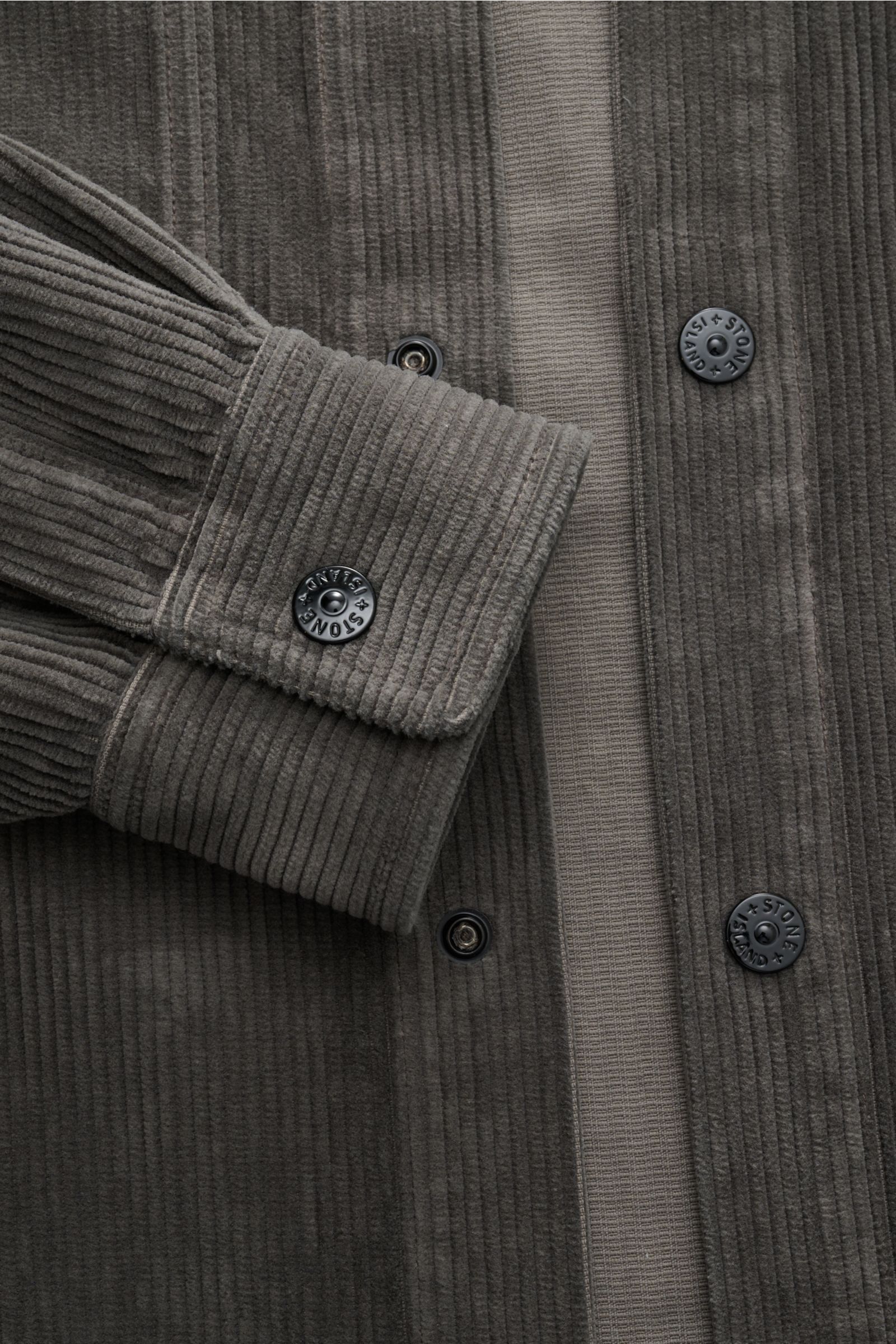 Nahaufnahme des Stone Island Cord Overshirt 'Organic Cotton Corduroy' dunkelgrau, zeigt Detailansicht der Druckknopfleiste und Manschette aus Bio-Baumwolle Cord.