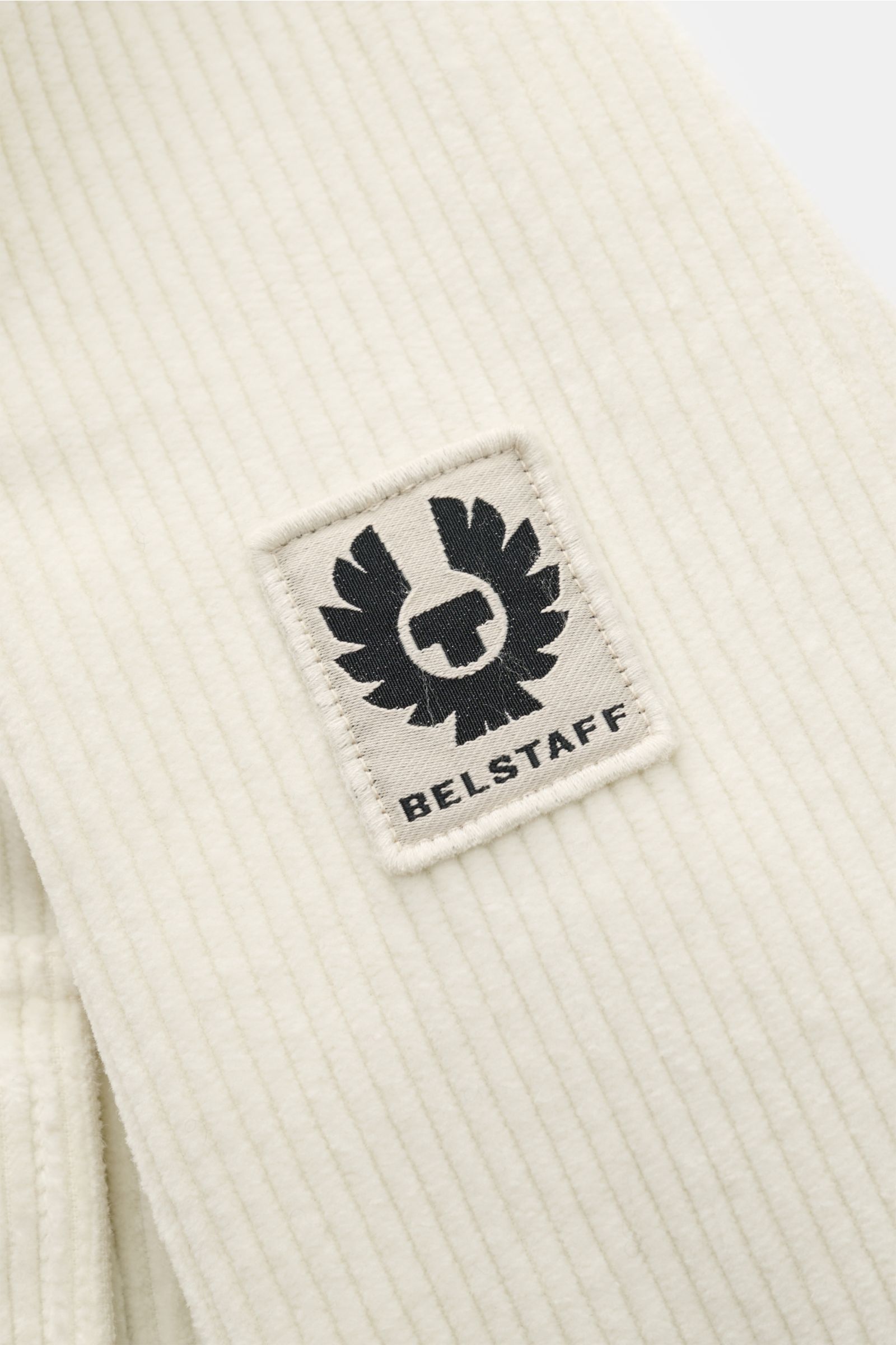 Close-up side view of the Belstaff Cord-Overshirt 'Fallgate' creme showing the tonal BELSTAFF logo patch on ribbed cotton cord fabric.

Cleaner Herbstlook von BELSTAFF: Das Overshirt 'Fallgate' aus robustem Baumwollcord bringt einen modernen Twist in I