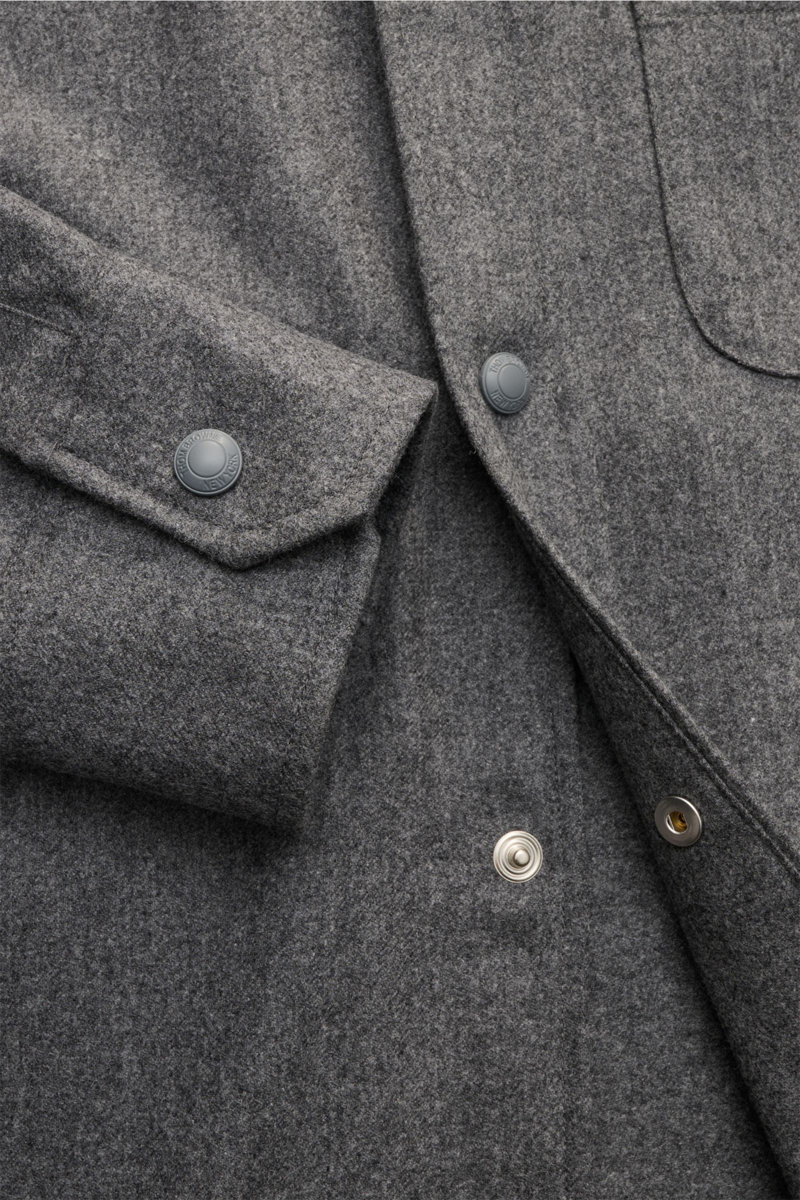 Nahaufnahme des Thom Browne Overshirts dunkelgrau meliert mit softem Griff, Wolle-Cashmere-Mix, Druckknopfleiste, Brusttasche und tonalen Ärmeln, schräg von oben fotografiert.